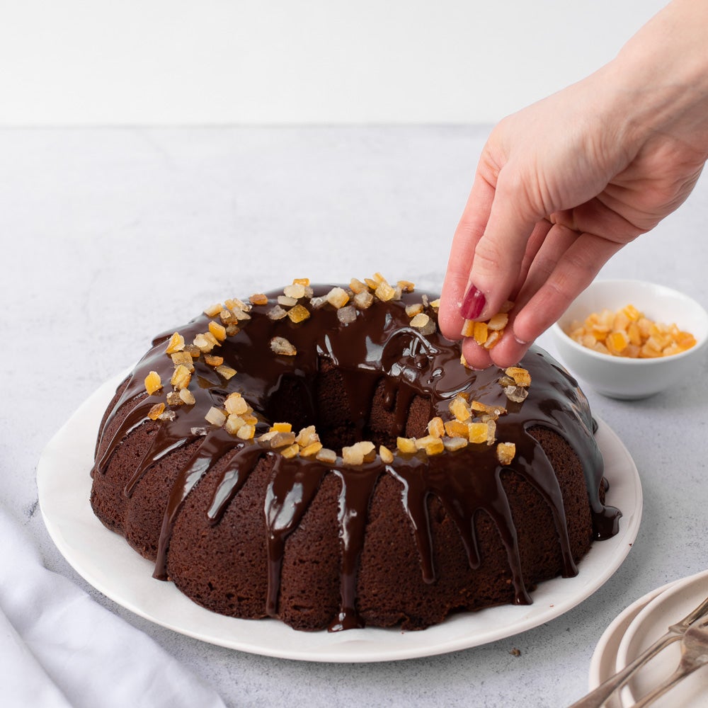 chocolate orange bundt cake on plate with chocolate drizzle on top with candid orange peel