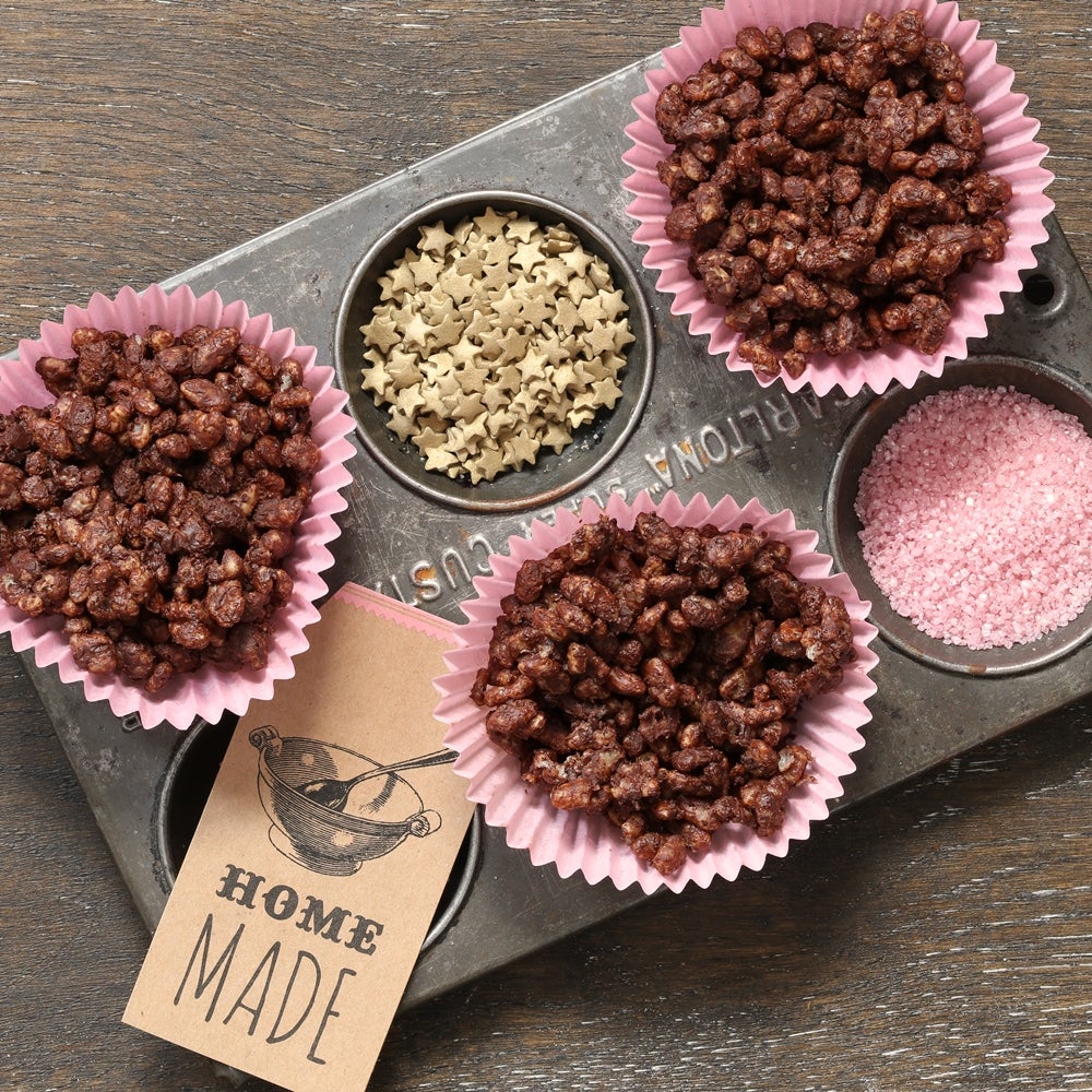 Chocolate rice crispy cakes in pink cupcake liners with decorative stars and pink glitter on a metal baking tray