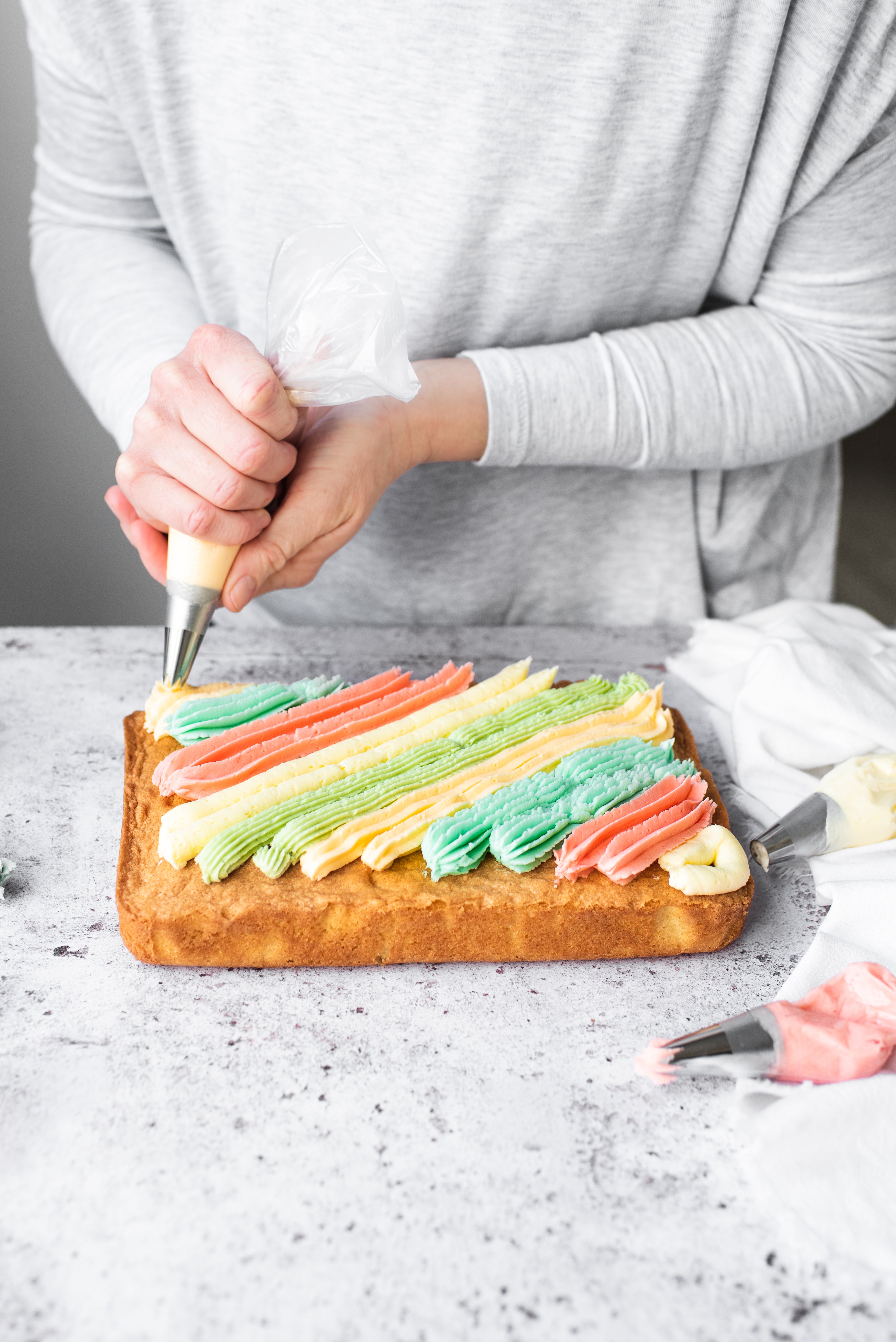rainbow buttercream being piped onto a traybake cake