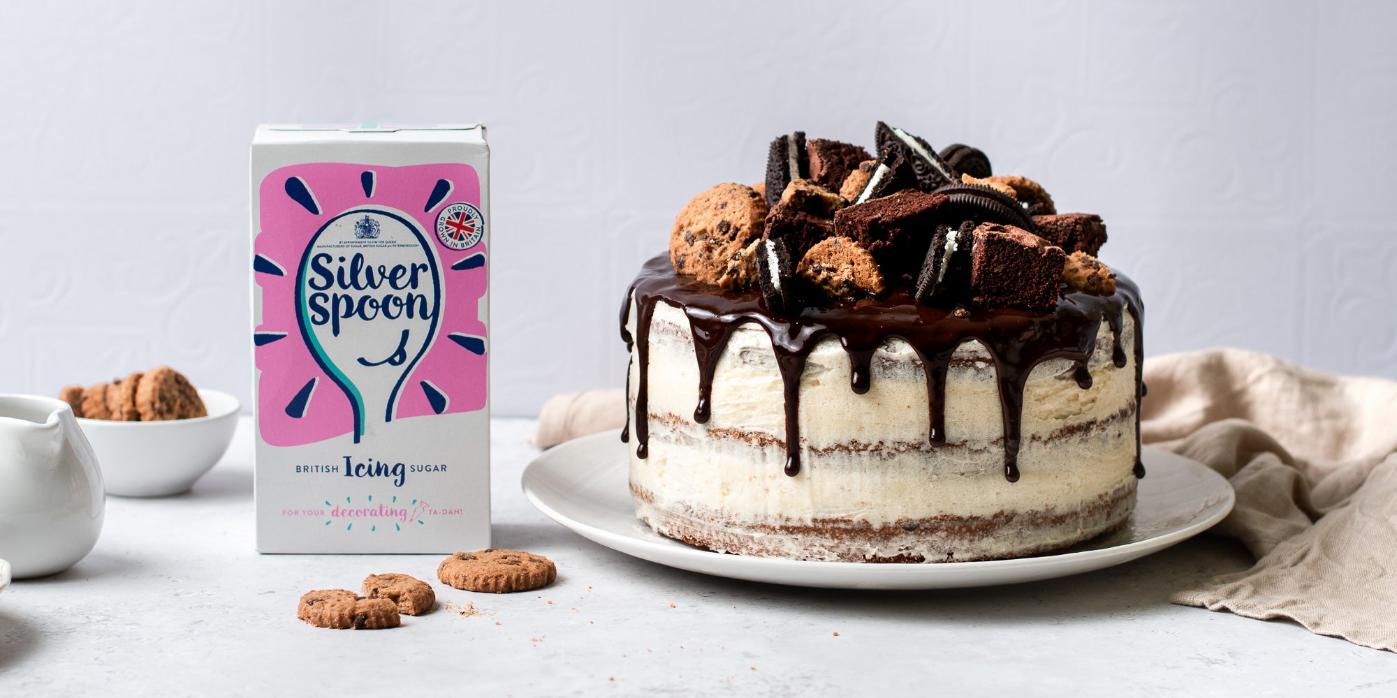Cookie, Oreo & Brownie Layered Cake with chocolate drip, next to a box of Silver Spoon icing sugar