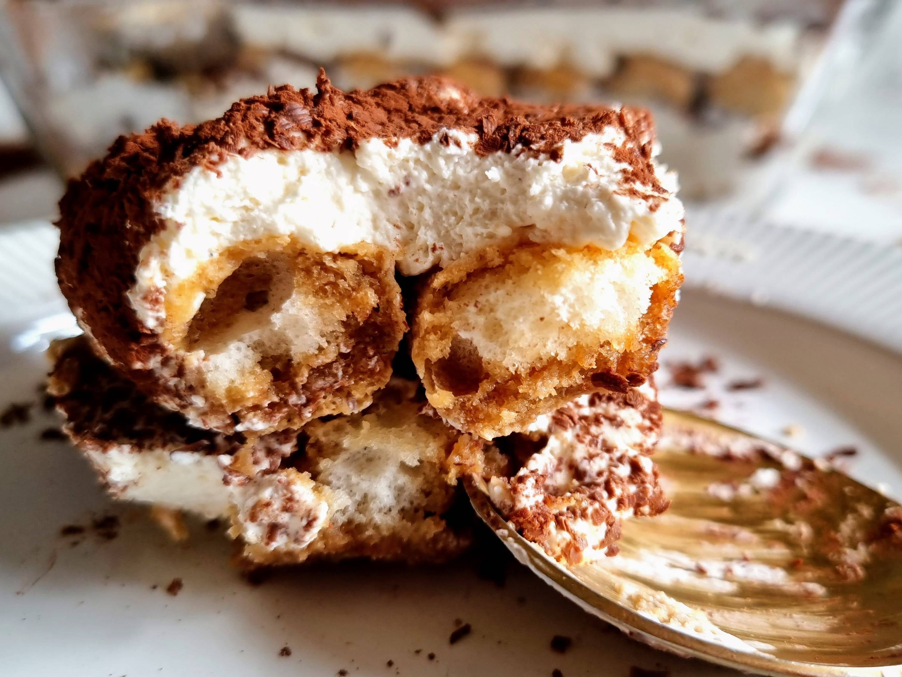 Close up of homemade tiramisu with sponge fingers, cream, cocoa powder on a white plate with a spoon