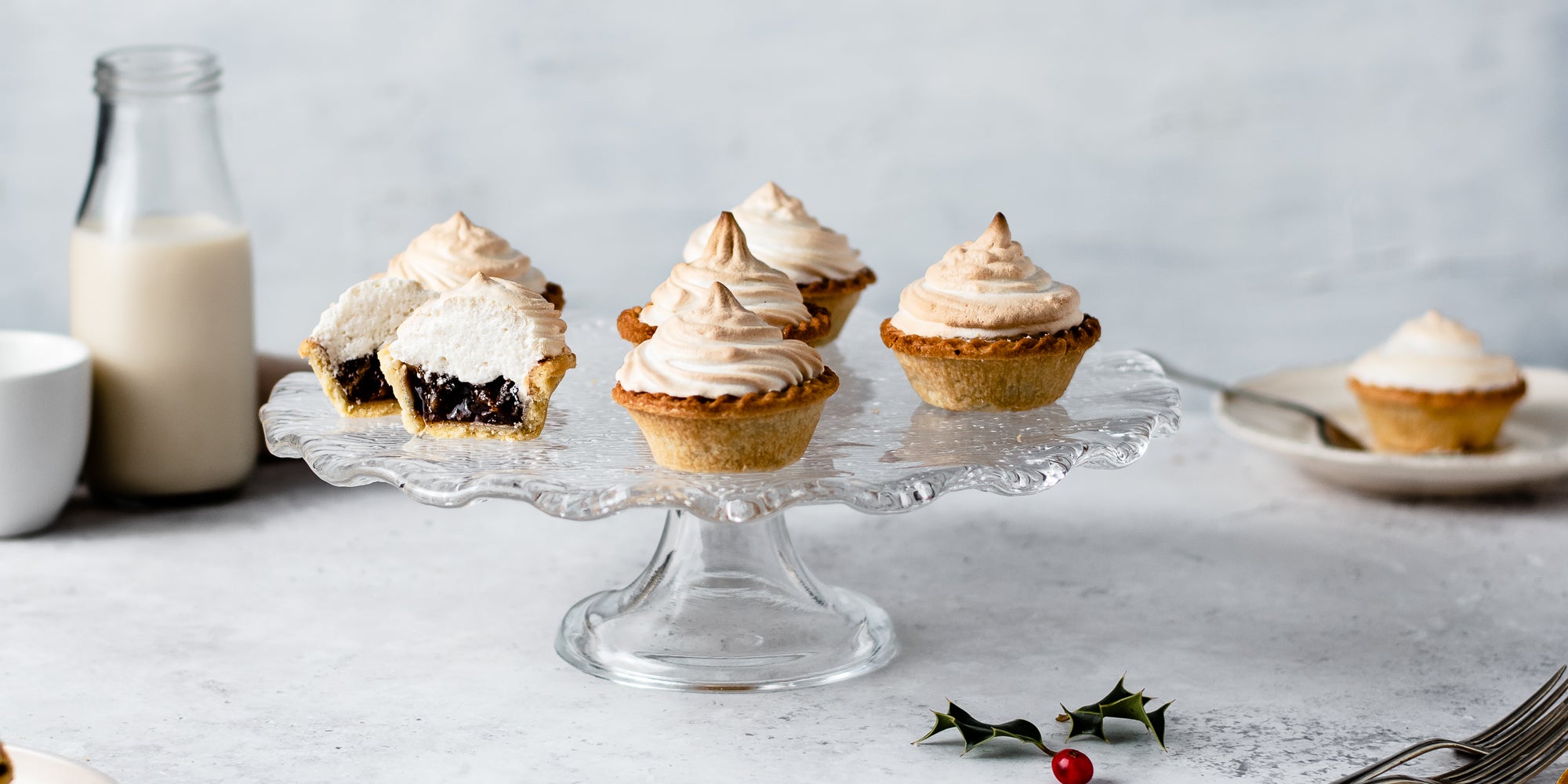 Meringue Topped Mince Pies on a glass cake stand with a close up of a mincepie cut in half showing the inside filled with mincemeat and meringue