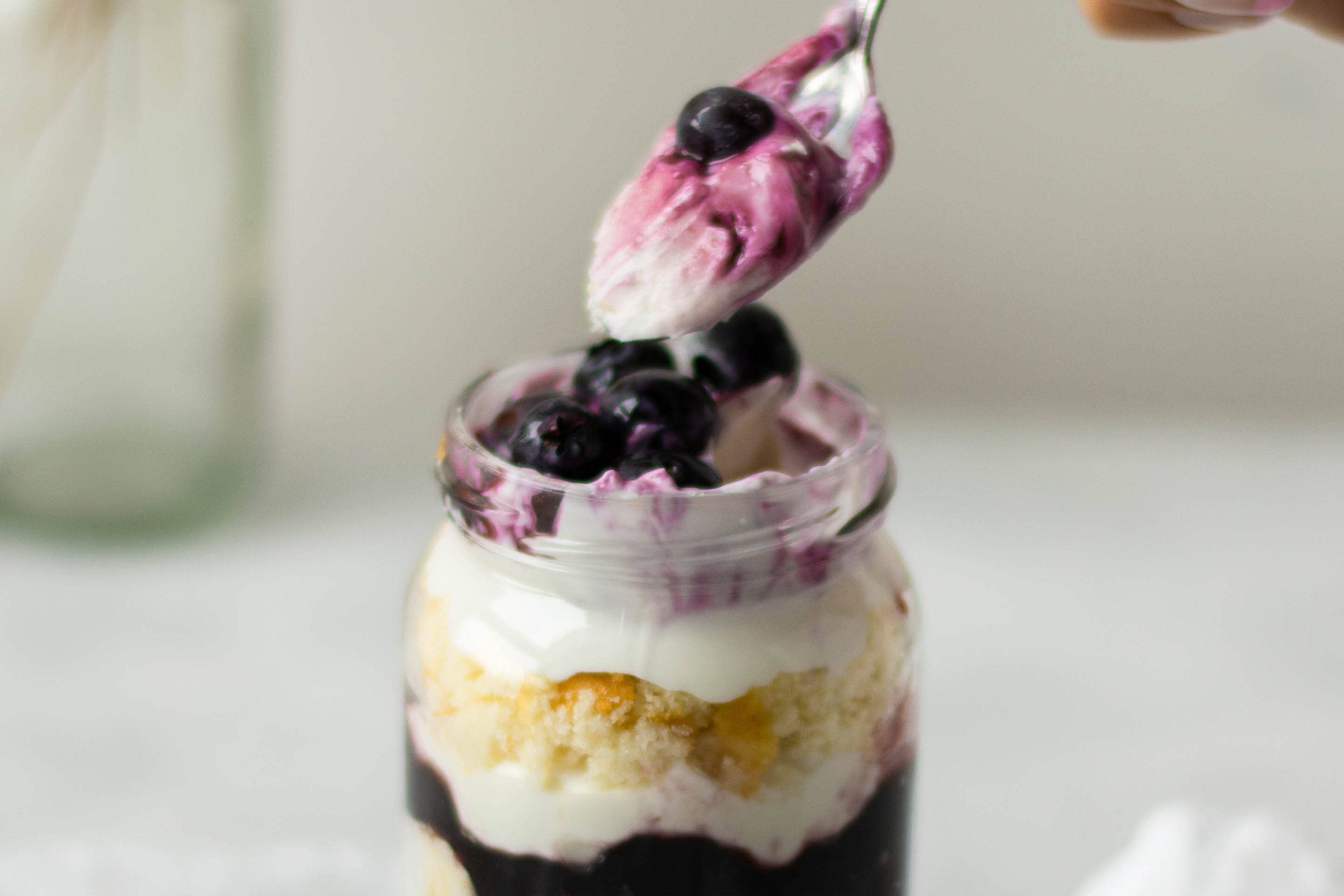 Close up of a spoonful of a Lemon & Blueberry Cake Jar with blueberry yoghurt and berries