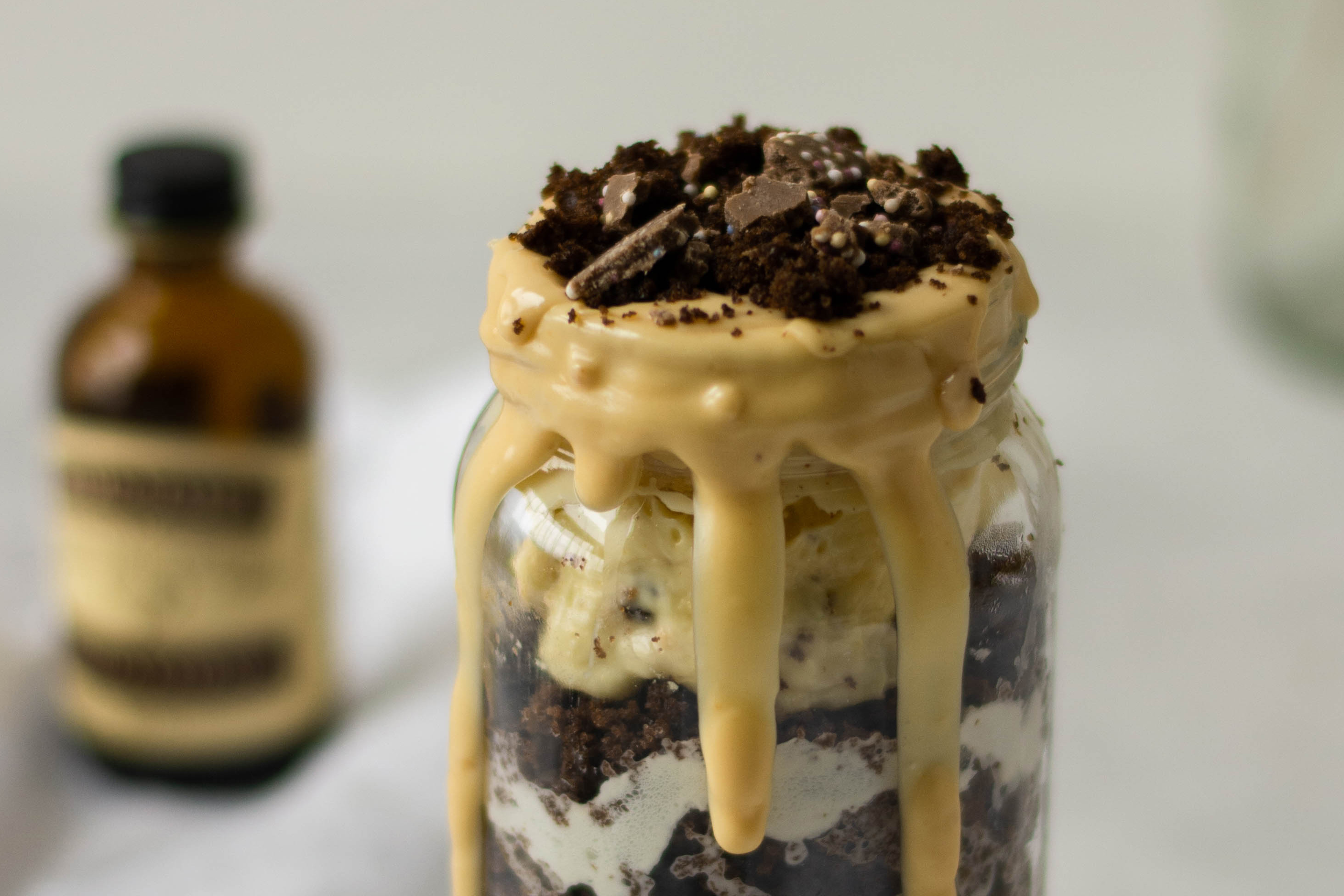 Close up of Bailey Jar Cake topped with cake crumbs and white chocolate, with a bottle of Nielsen-Massey Vanilla Extract in the background