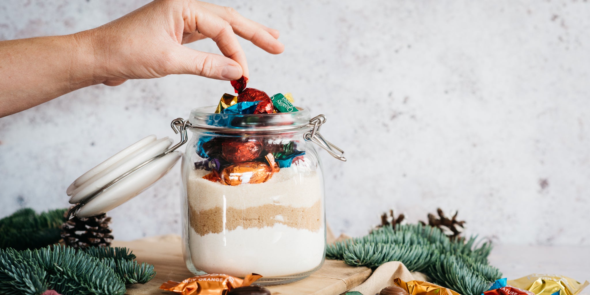 Christmas Cookies in a Jar with a hand reaching to pick a quality street out of the top of the jar 