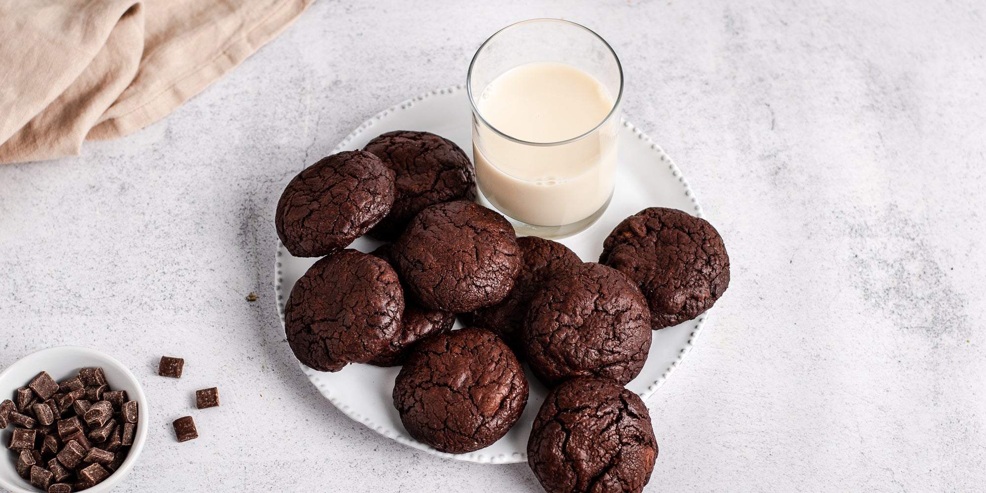 A batch of Chocolate Brownie Cookies on a plate, next to a glass of milk