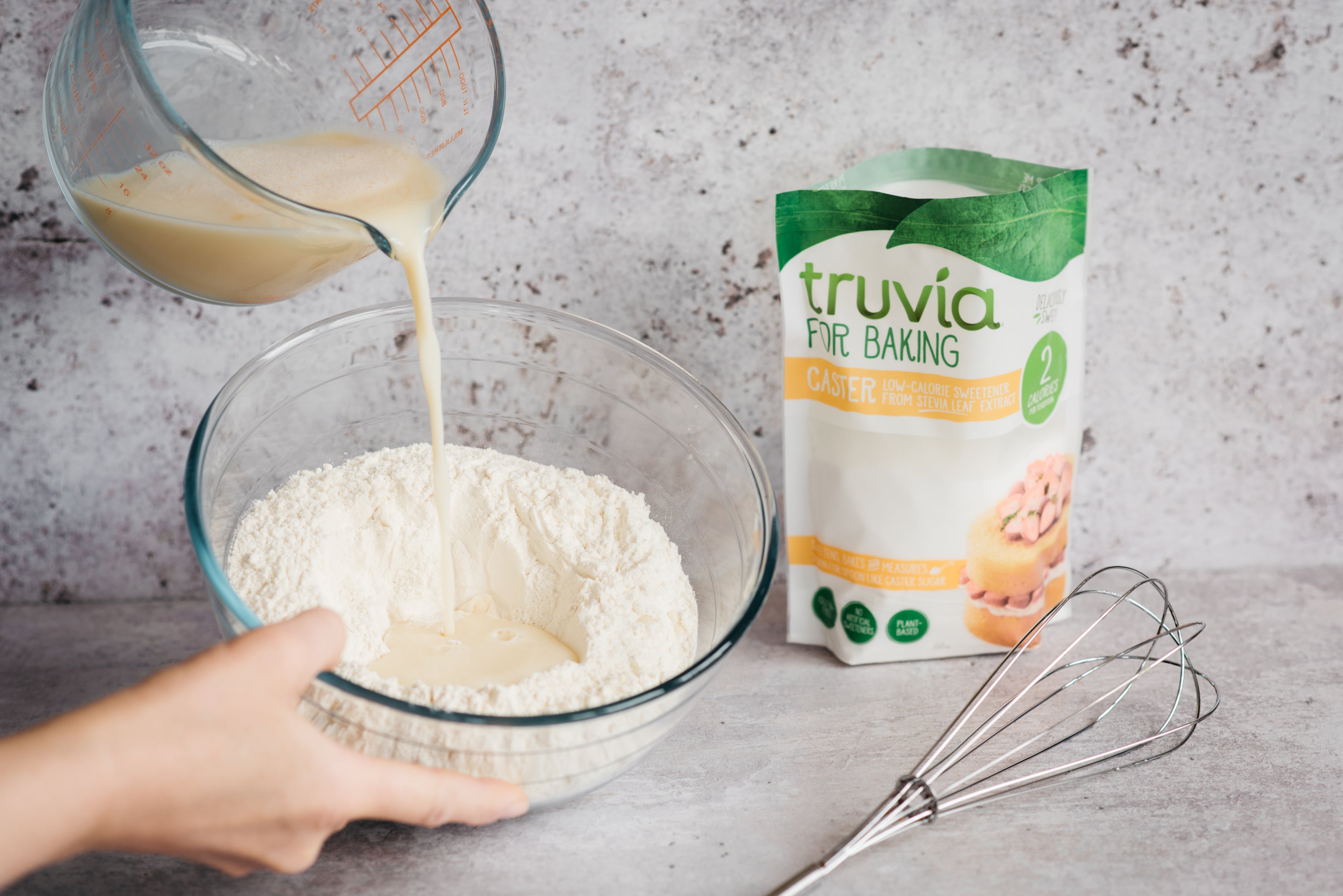 Wet ingredients being poured into dry, with a pack of Truvia for Baking Caster next to the bowl