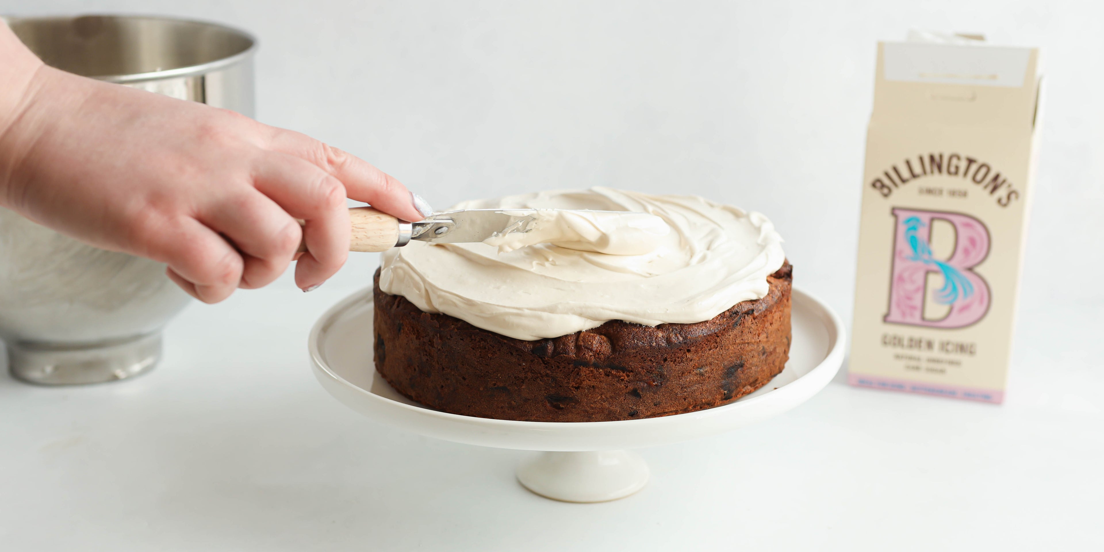 Fruit Cake being smothered with Billington's Golden Icing Sugar buttercream with a hand holding an offset spatula