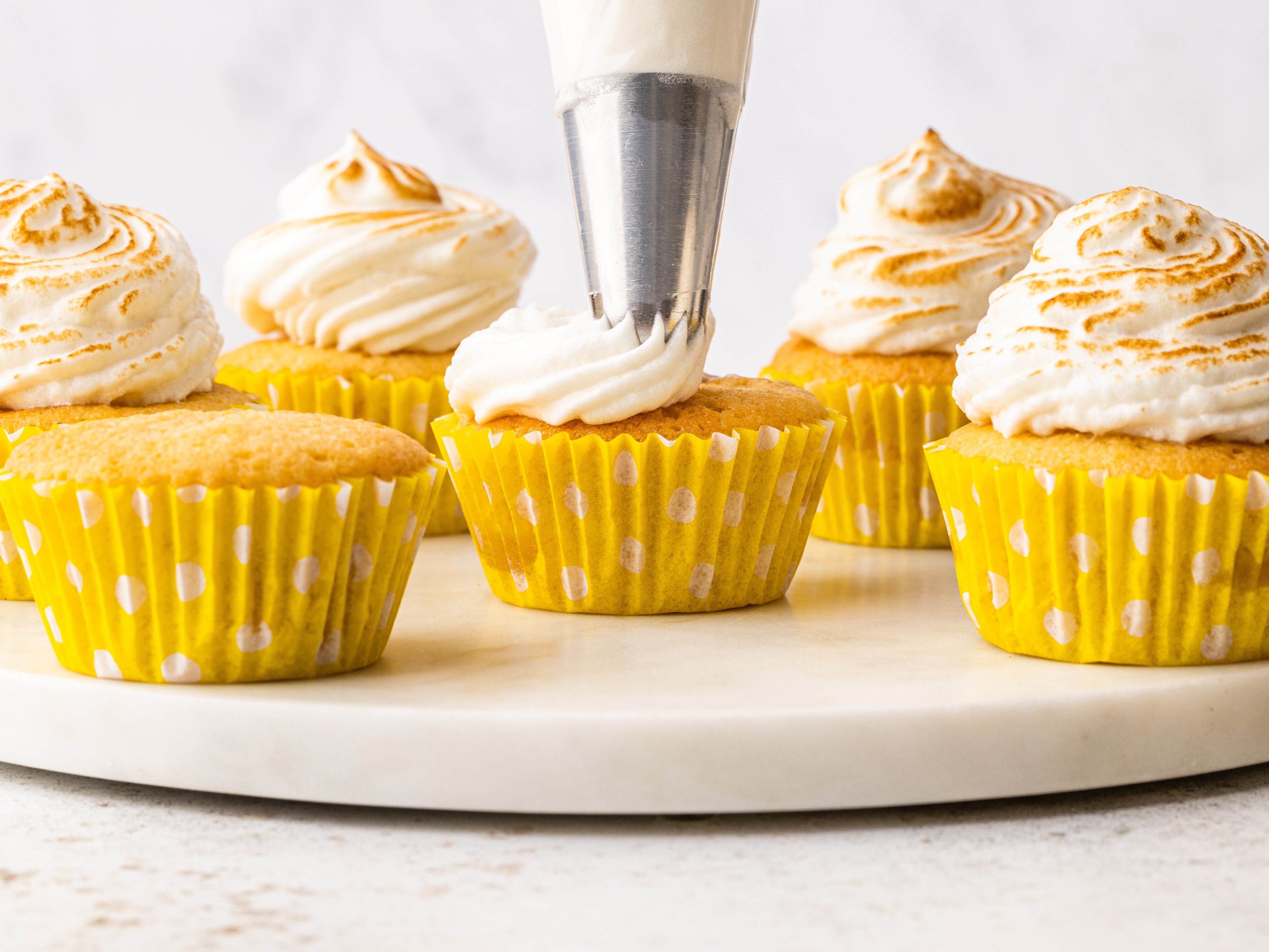 Meringue being piped on top of cupcakes in yellow cupcake cases