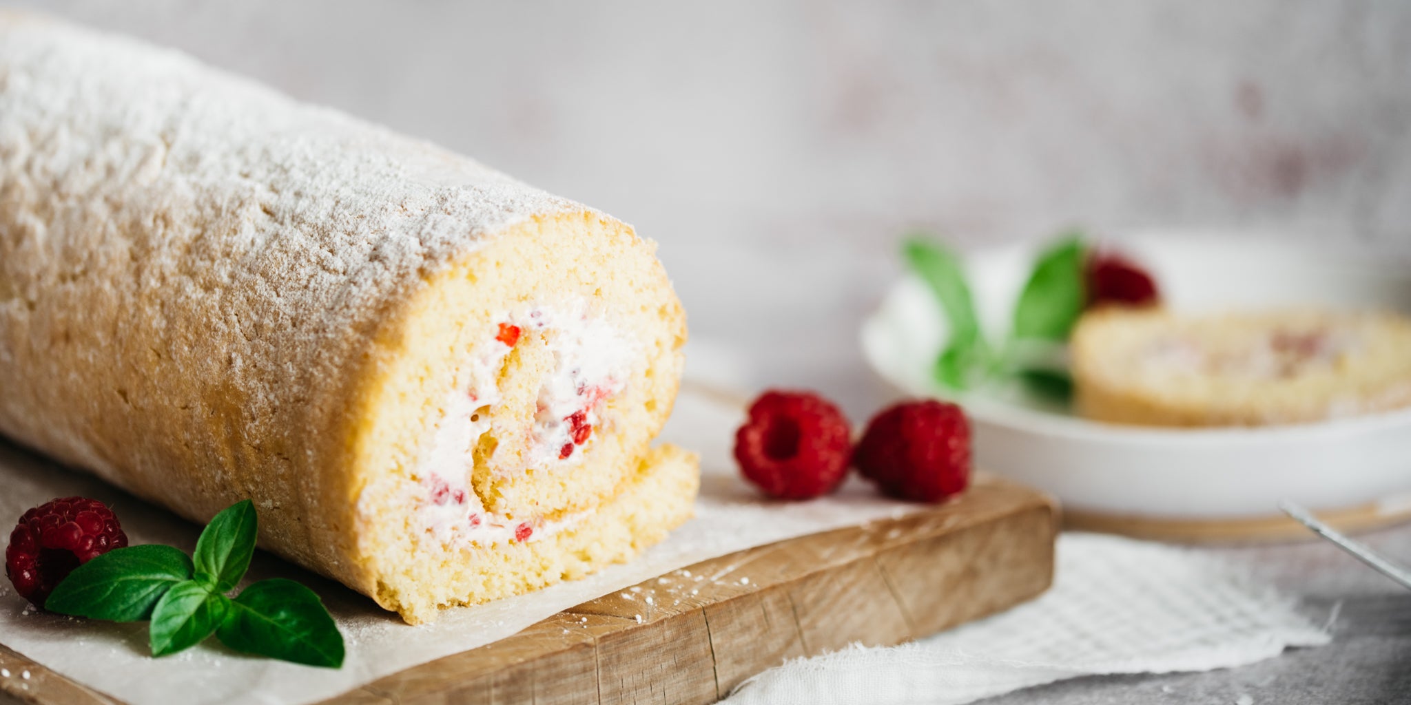 Raspberry roulade on a wooden board surrounded by raspberries