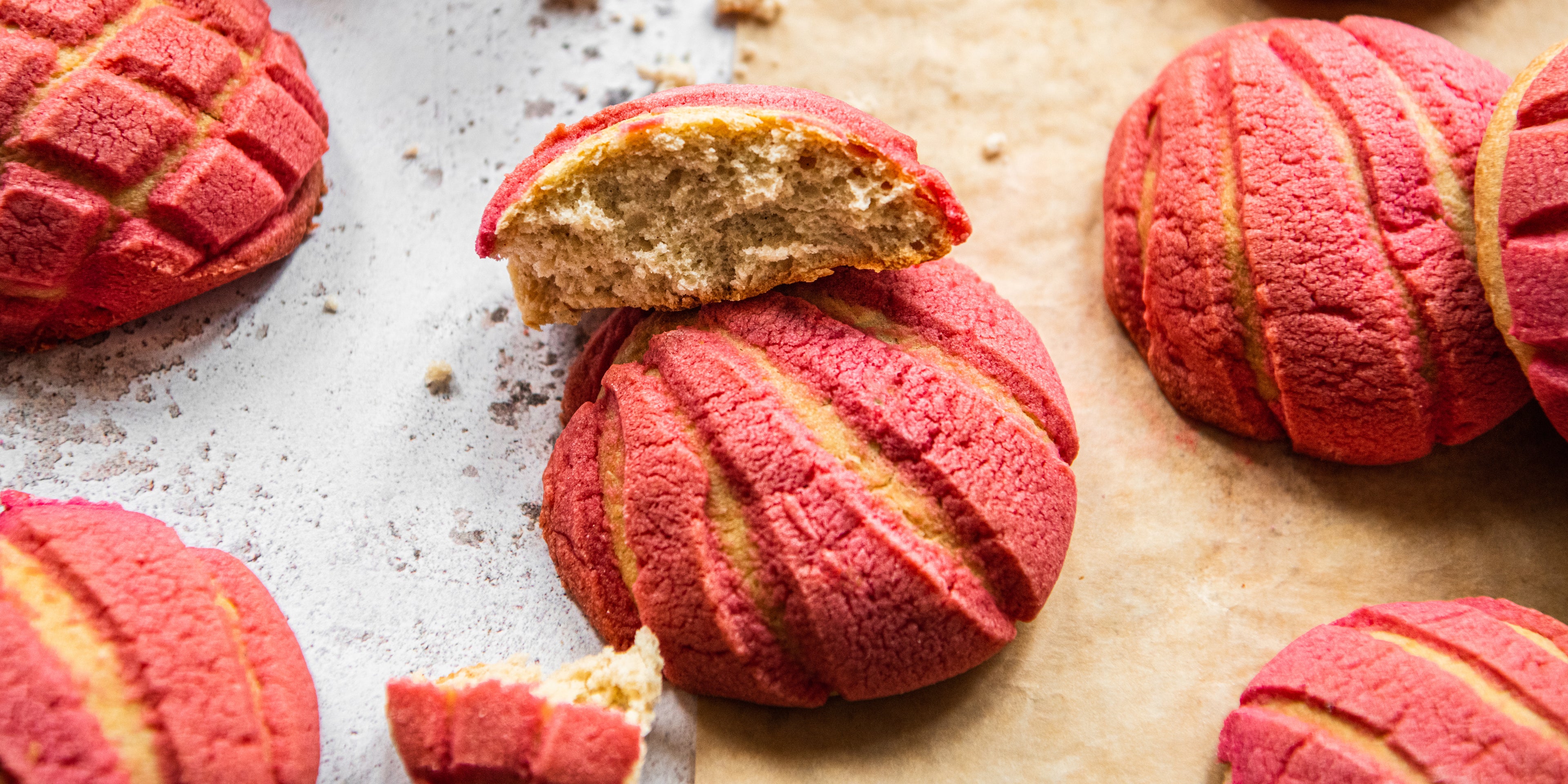 Close up of Conchas, with patterned pink tops broken open to show the golden insides and crumbly texture.