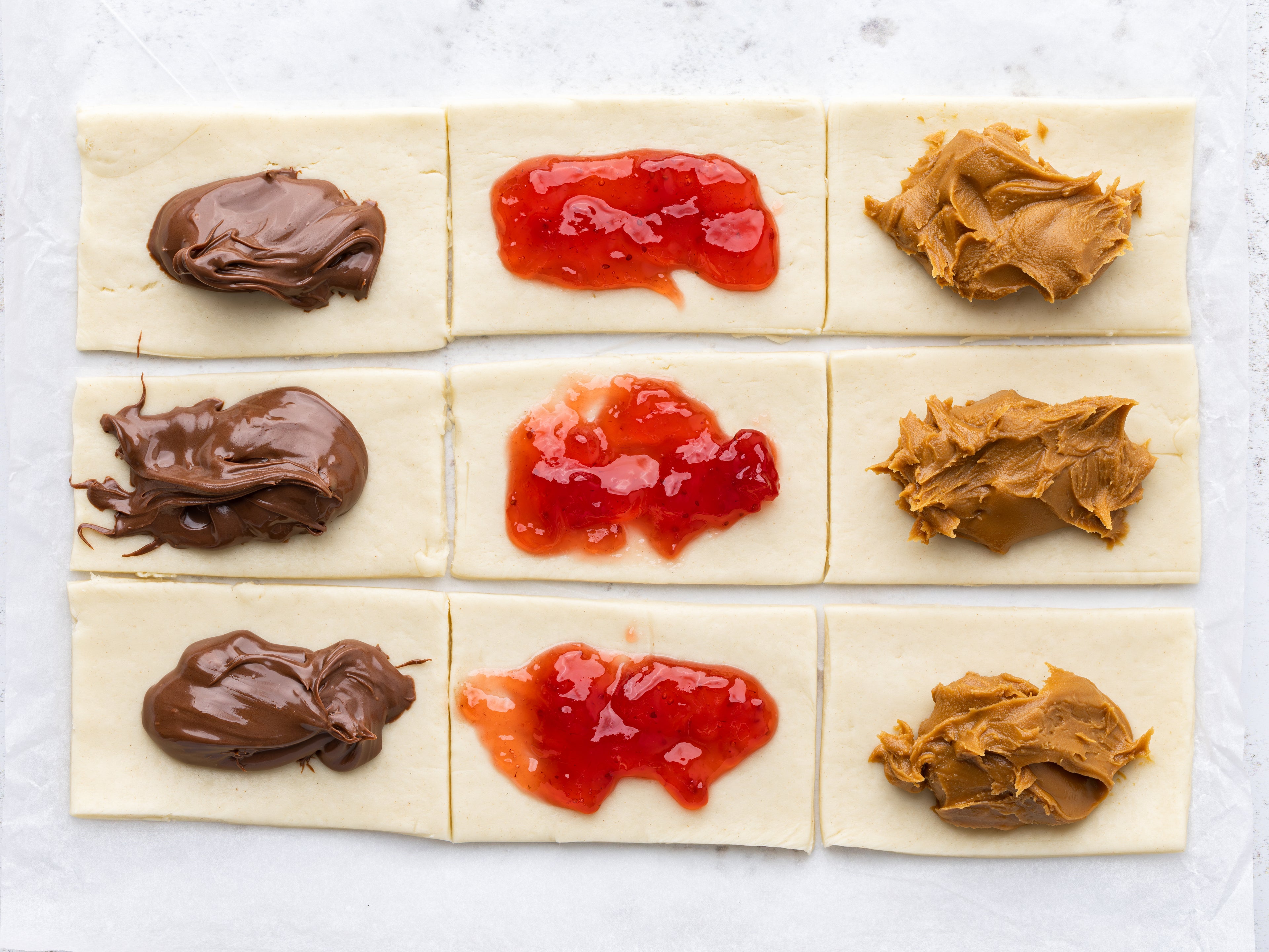 Pastry cut into 9 squares with blobs of jam, chocolate and biscoff spread in each one