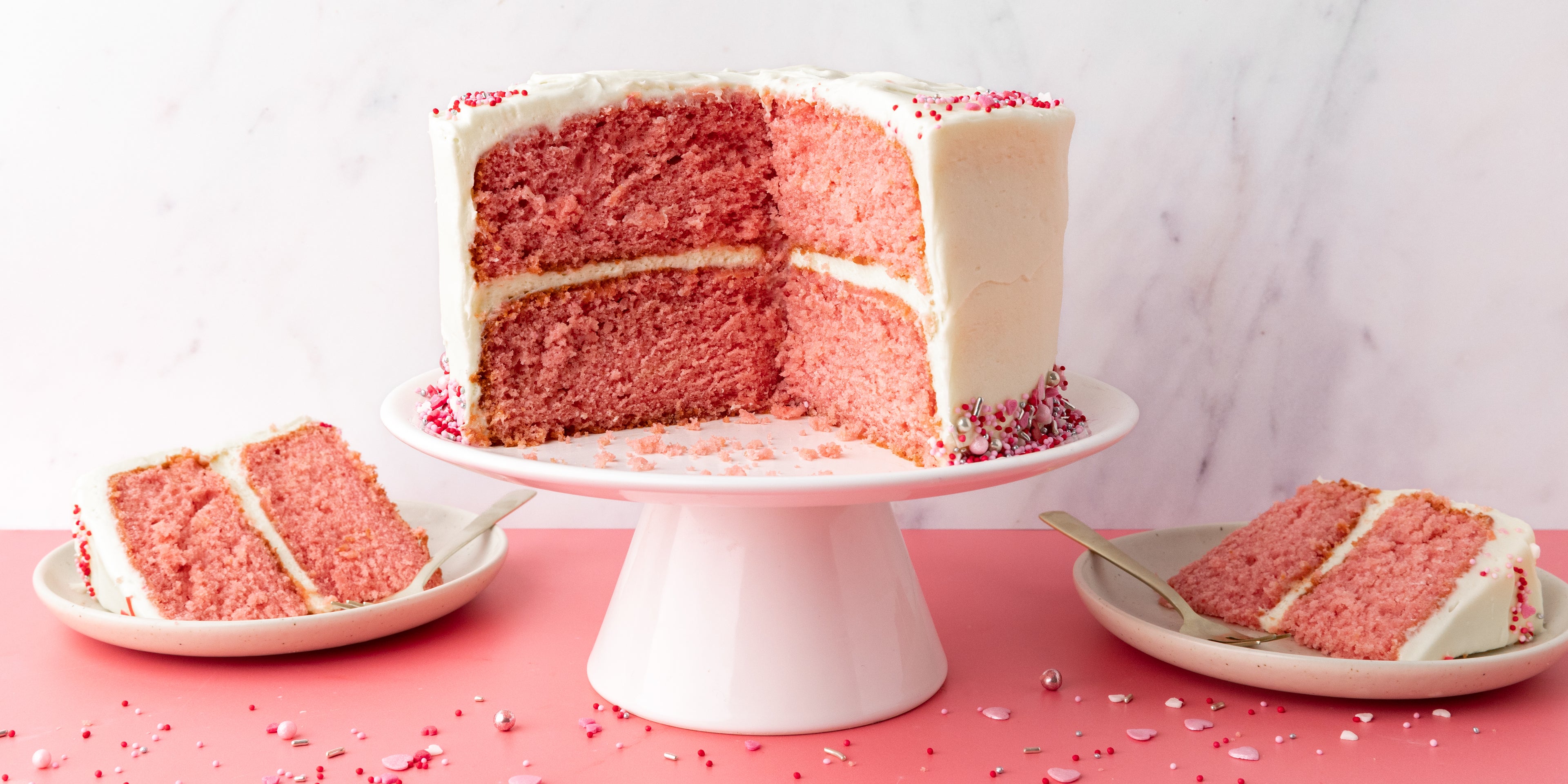 Cake sliced open to show a pink centre and coated in a white buttercream with pink sprinkles