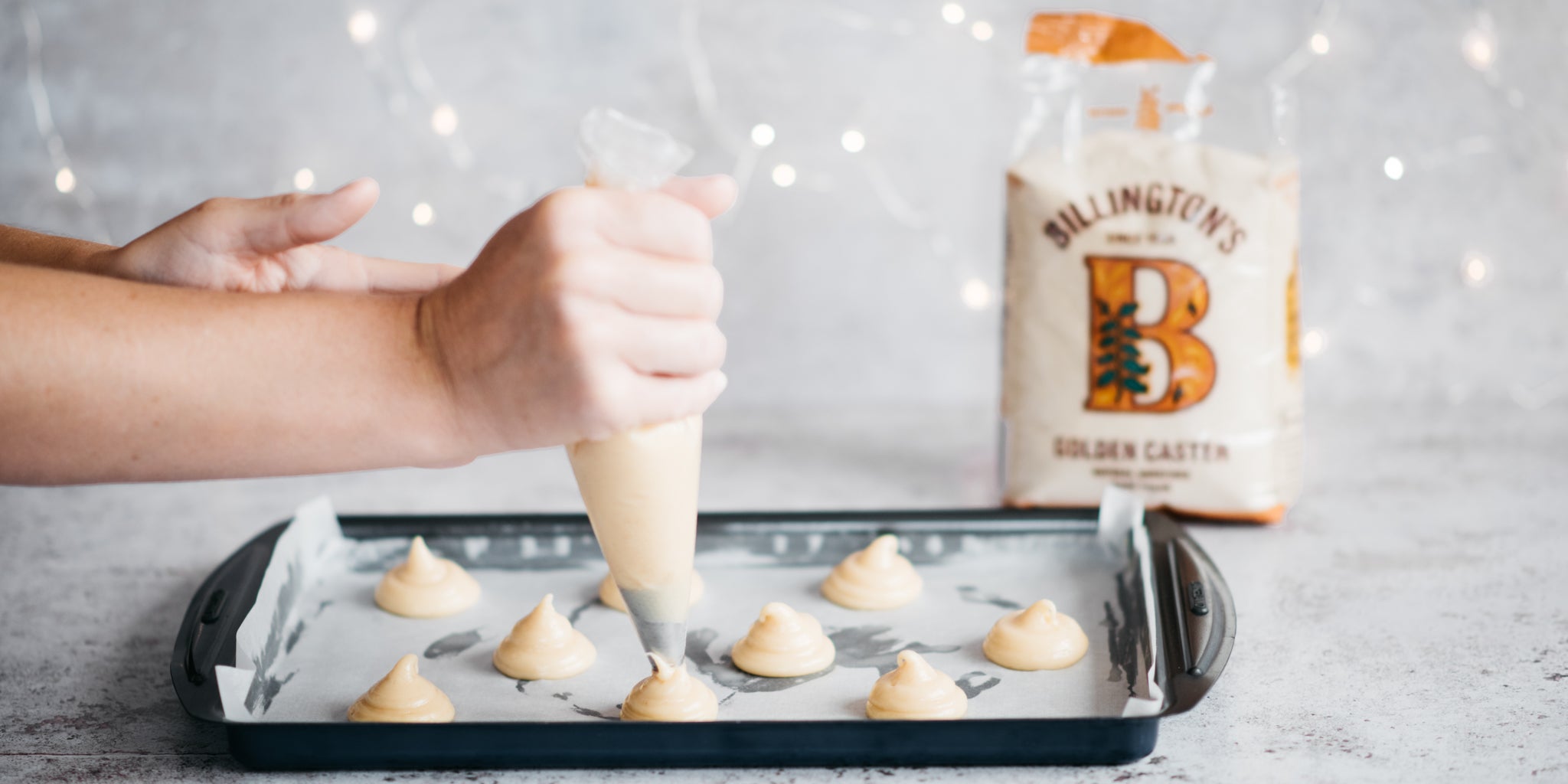 Hand piping choux pastry dough onto baking tray with sugar in background