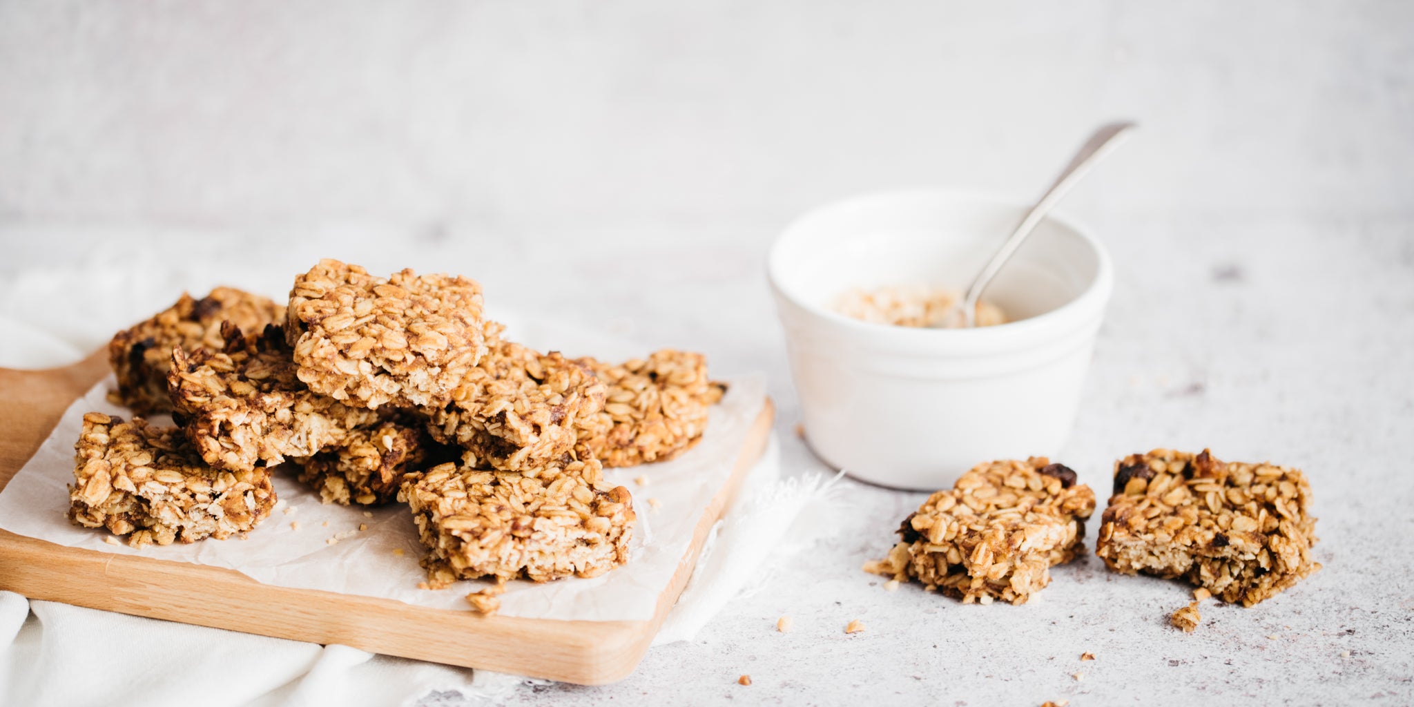 Stack of flapjacks on wooden board. White bowl and torn apart flapjack beside