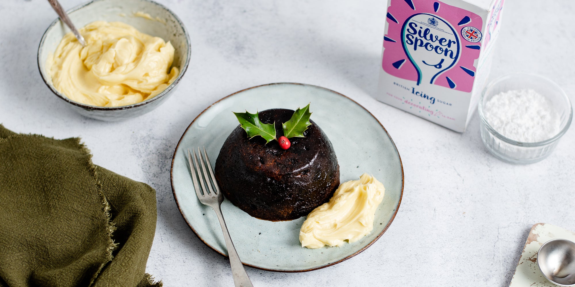 Top view of a dollop of Brandy Butter next to a christmas pudding and a box of silver spoon icing sugar in the background