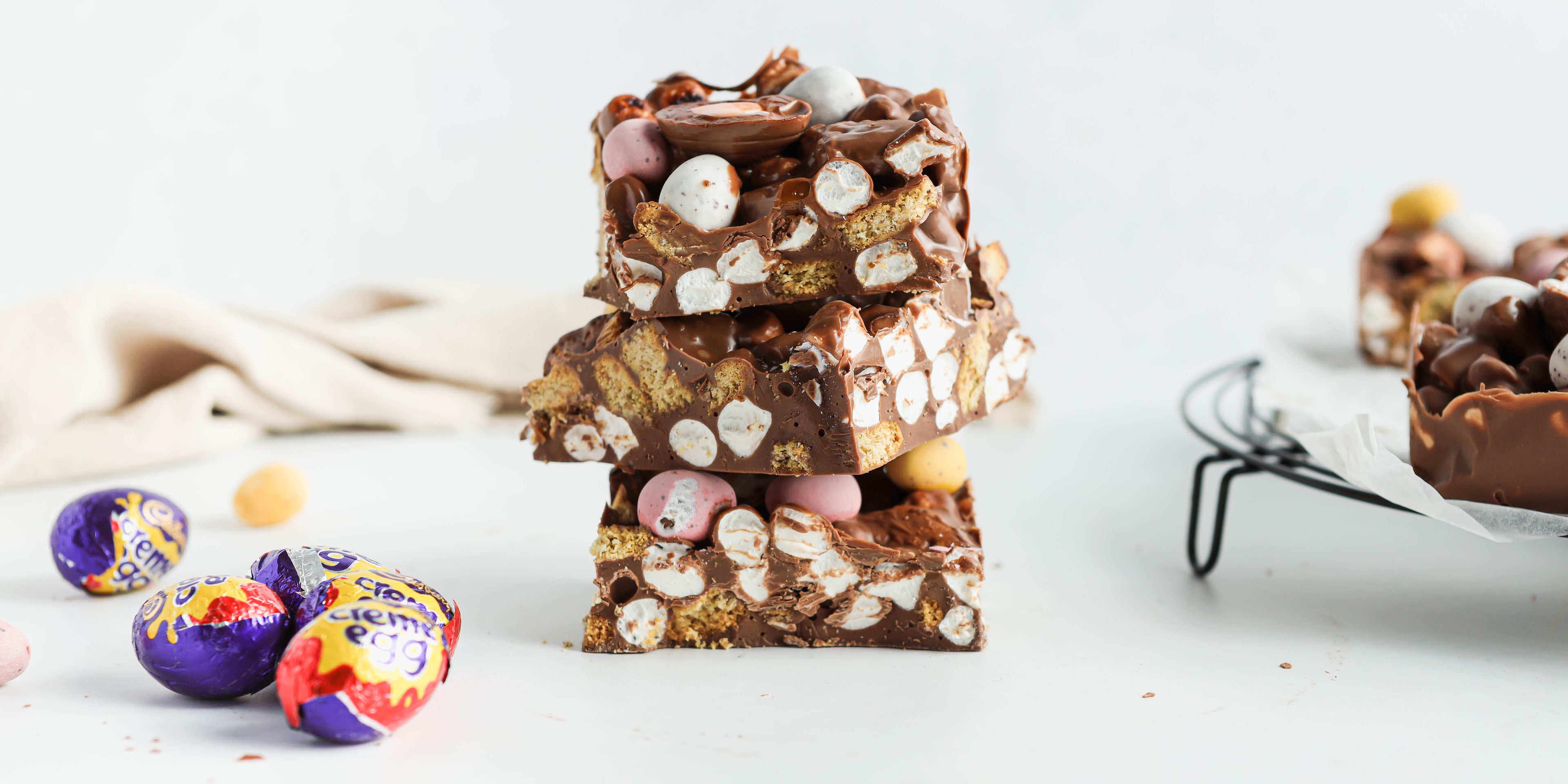 Close up of a stack of Easter Egg Rocky Road slices, showing the inside of the rocky road filled with mini eggs, marshmallows and biscuits.