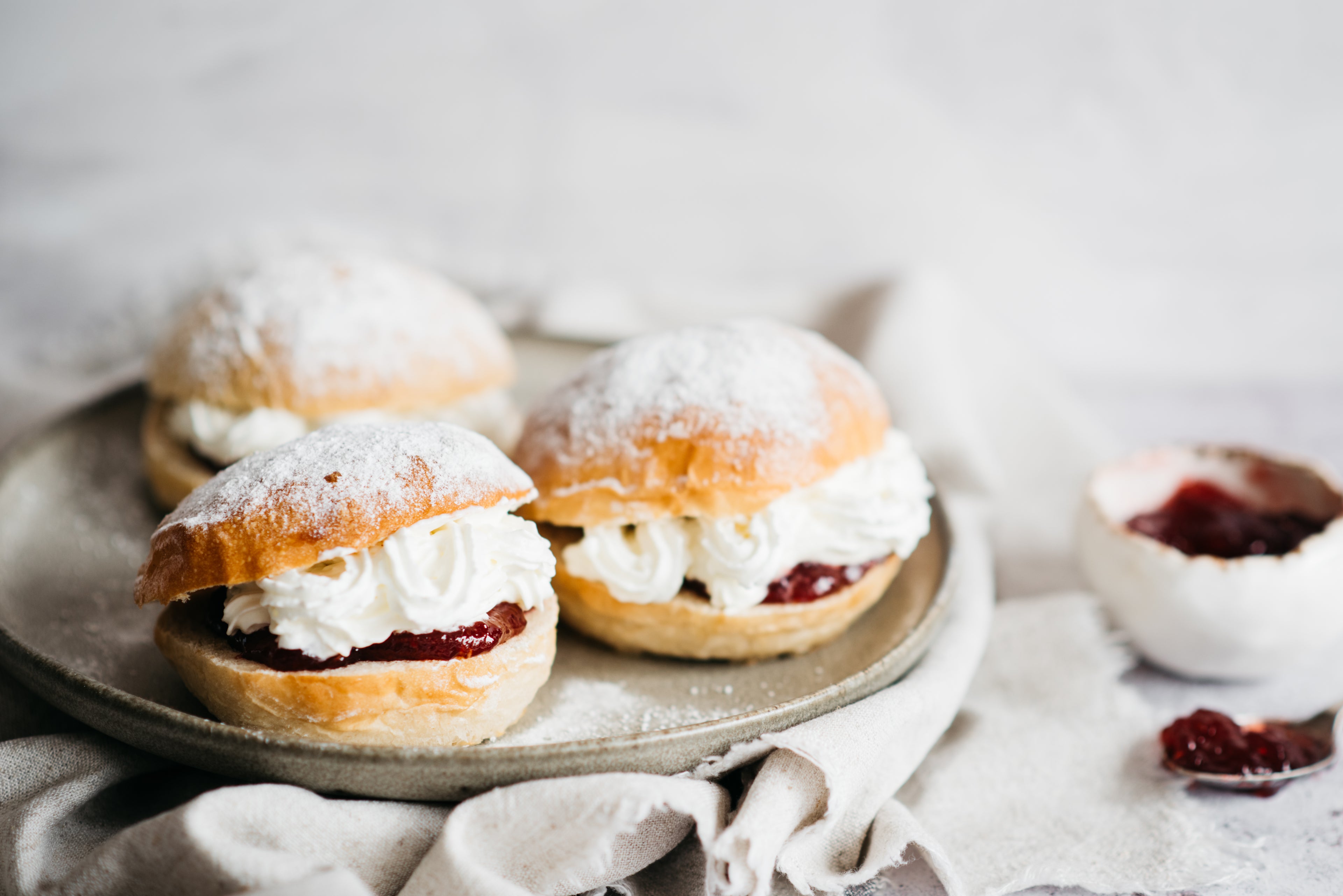 Close up of Devonshire Splits on a plate, filled with cream and jam, with a bowl of jam in the background