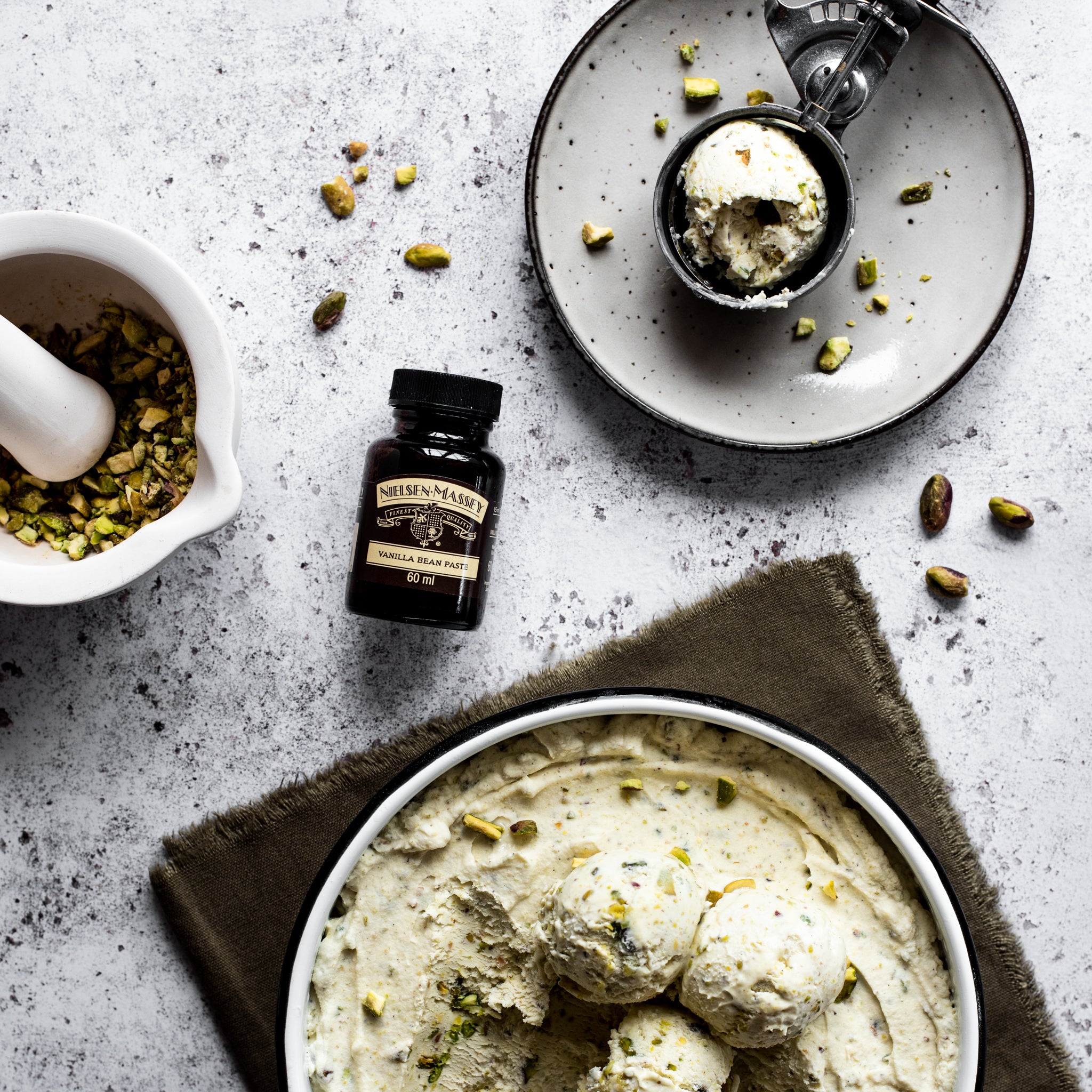 Bowl of pistachio ice cream, surrounded by crushed pistachios and a bottle of vanilla essence 