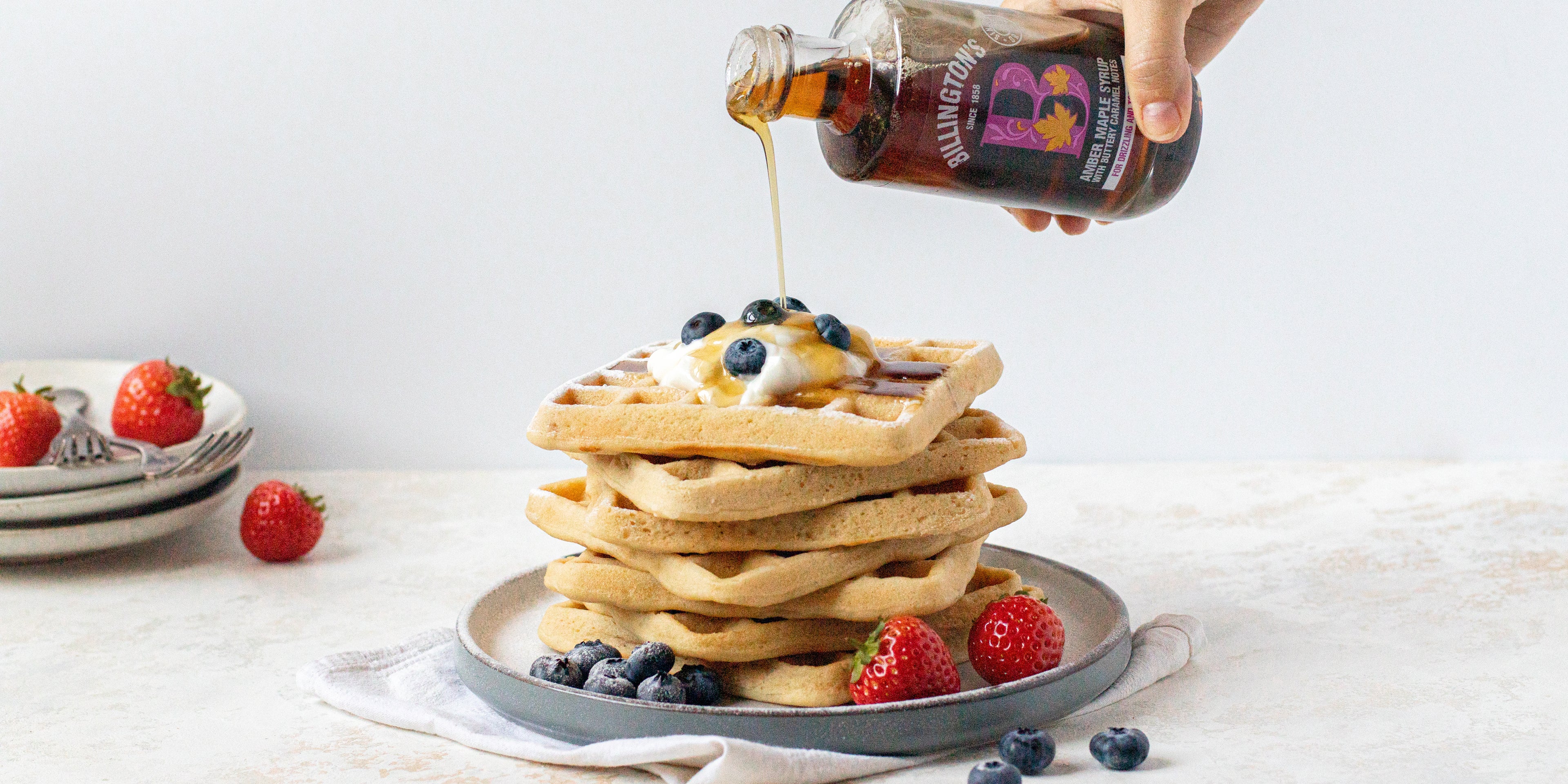 A stack of vegan gluten free waffles with a hand pour Billington's syrup over