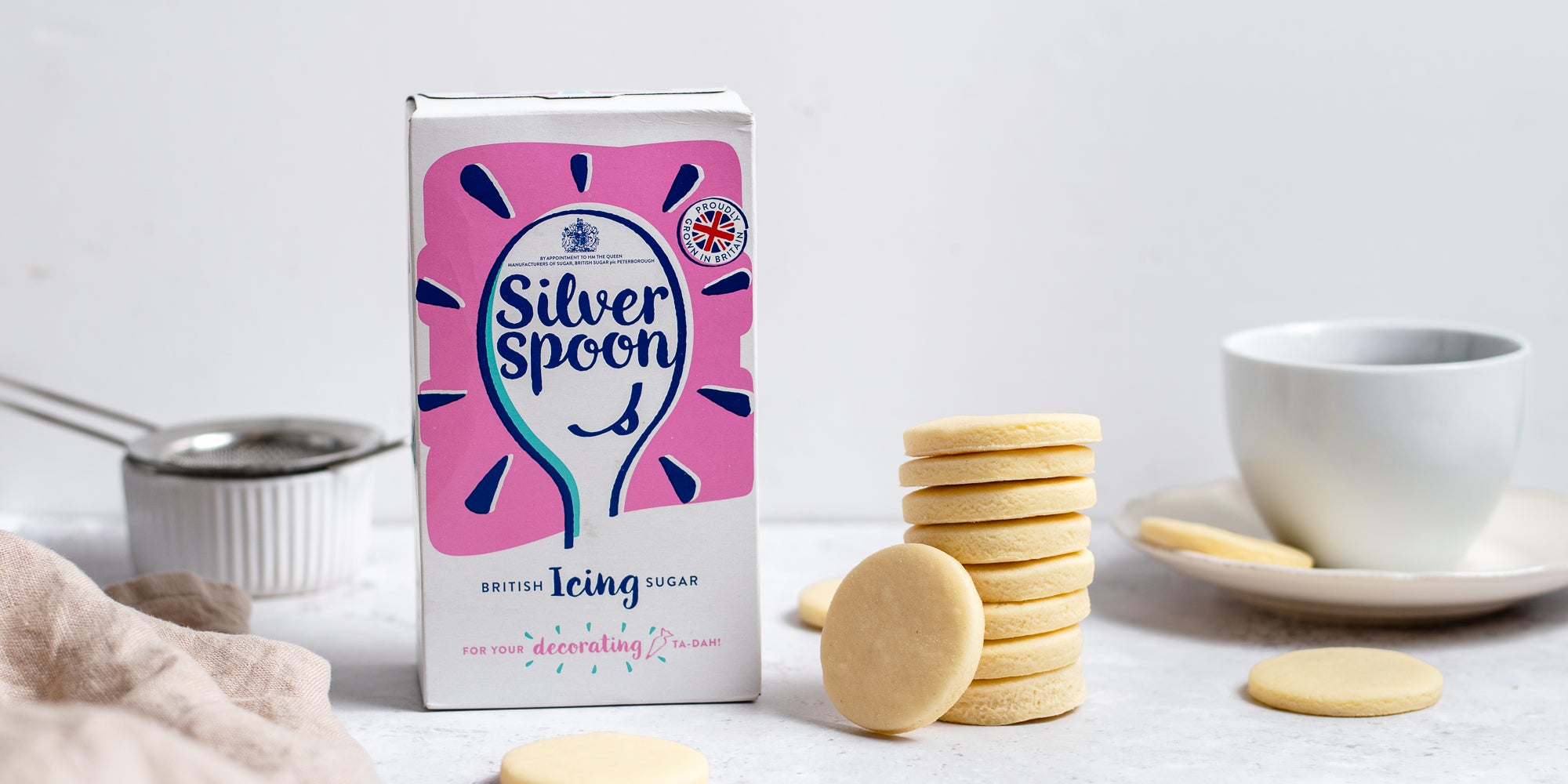 Side on view of a tower of vegan shortbread next to a cup of tea and silver spoon icing sugar