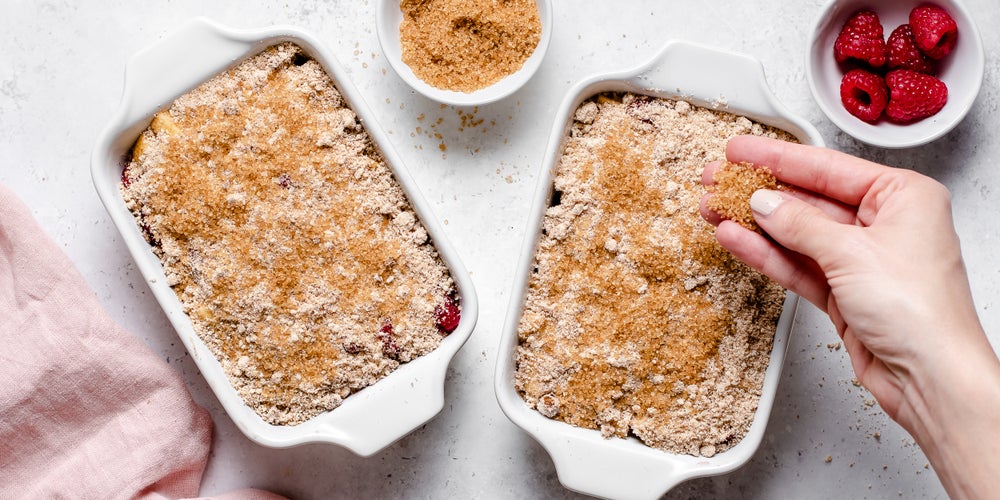 Apple & Raspberry Crumbles being hand sprinkled with golden sugar for a crunchy top
