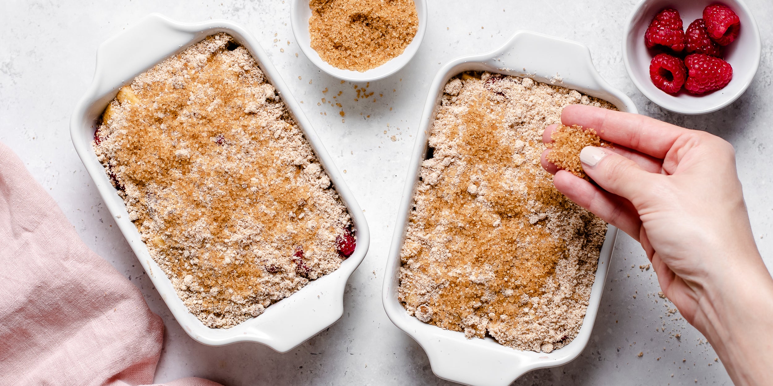 Apple & Raspberry Crumbles being hand sprinkled with golden sugar for a crunchy top 