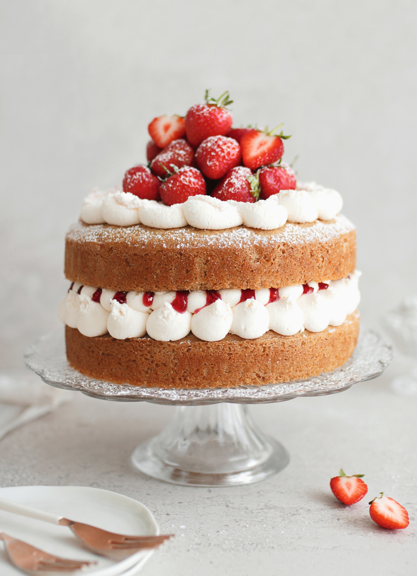 Close up of Vegan Victoria Sponge Cake on a cake stand, piped with vegan buttercream and topped with fresh berries