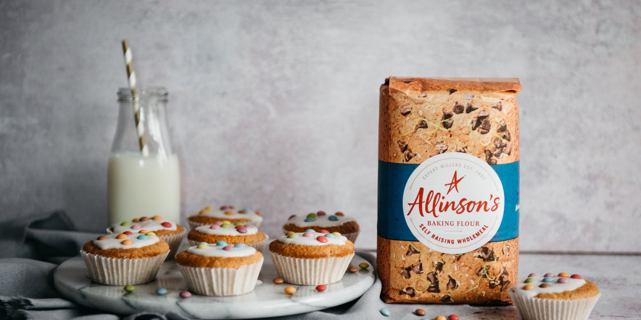 Wholemeal Fairy Cakes next to a bag of Allinson's Wholemeal Flour, with a glass bottle of milk in the background