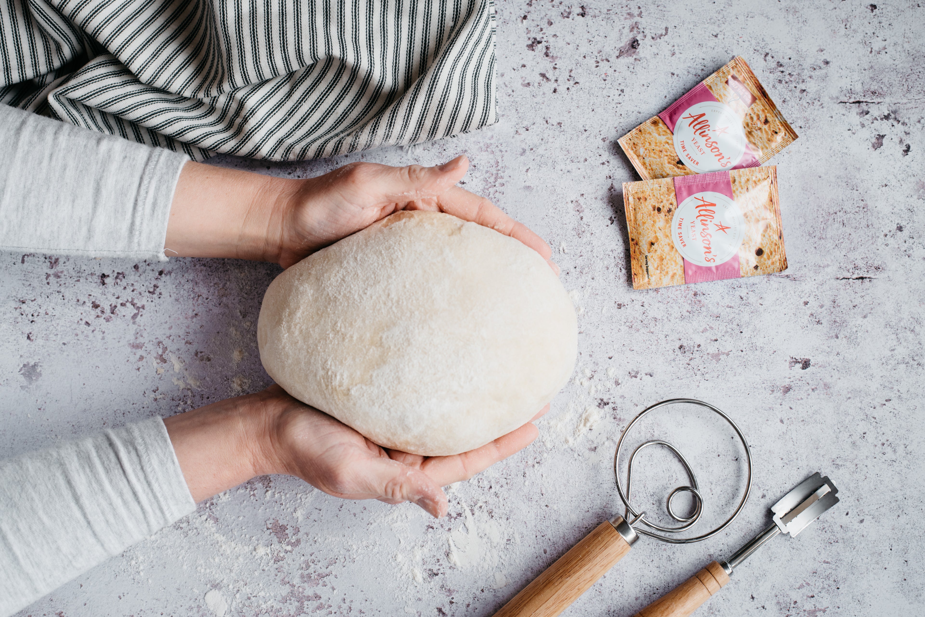 Bread dough being cupped by two hands next to some packets of yeast