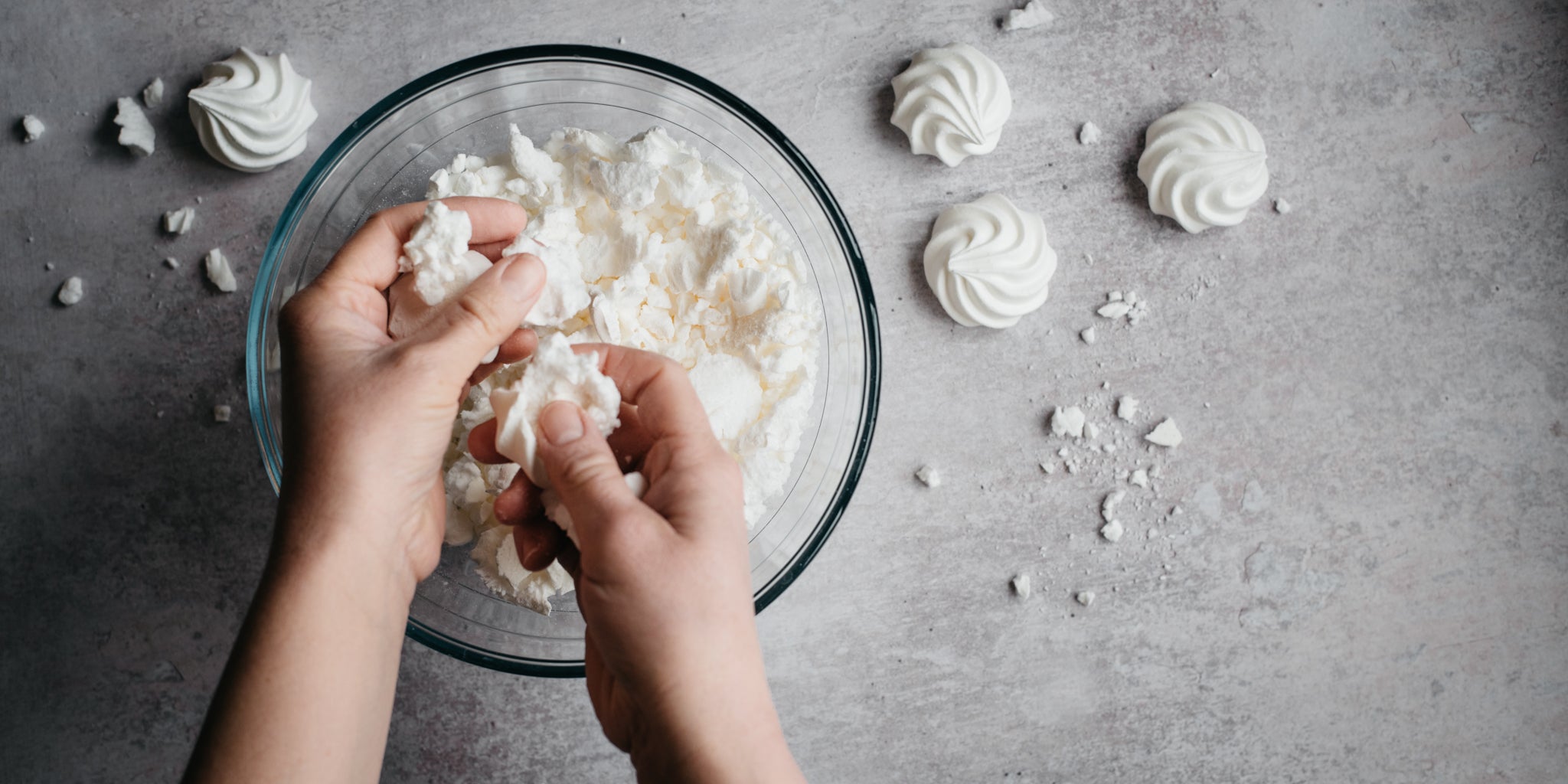 Top view of hands crumbling fresh meringue into the Eton Mess Trifle