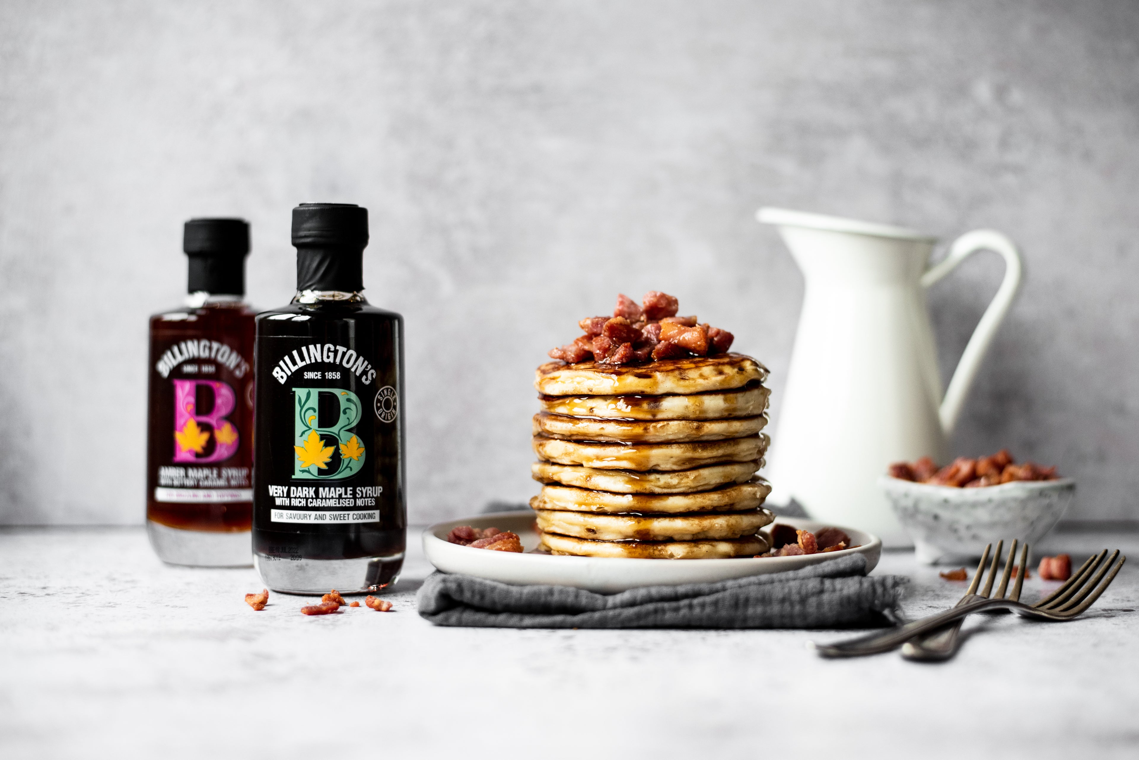 Pancake stack with bacon/ Maple syrup bottles and jug in background
