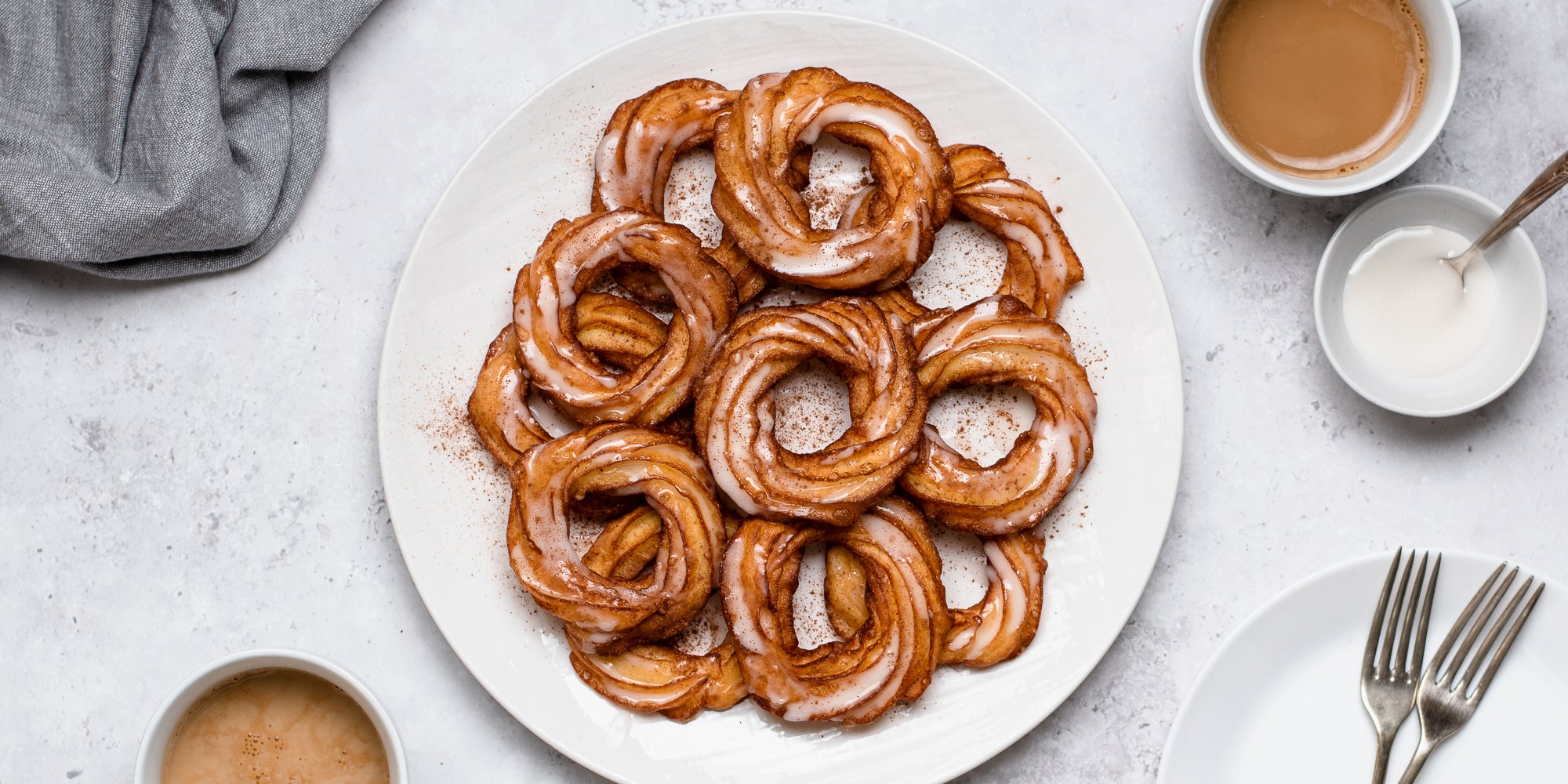 Top view of Apple Cider Crullers on a plate, drizzled with icing and dusted with cinnamon