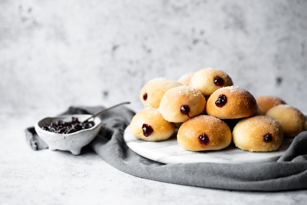 A marble round plate with a pile of freshly baked jam doughnuts sat on top, next to a small dish of red jam.