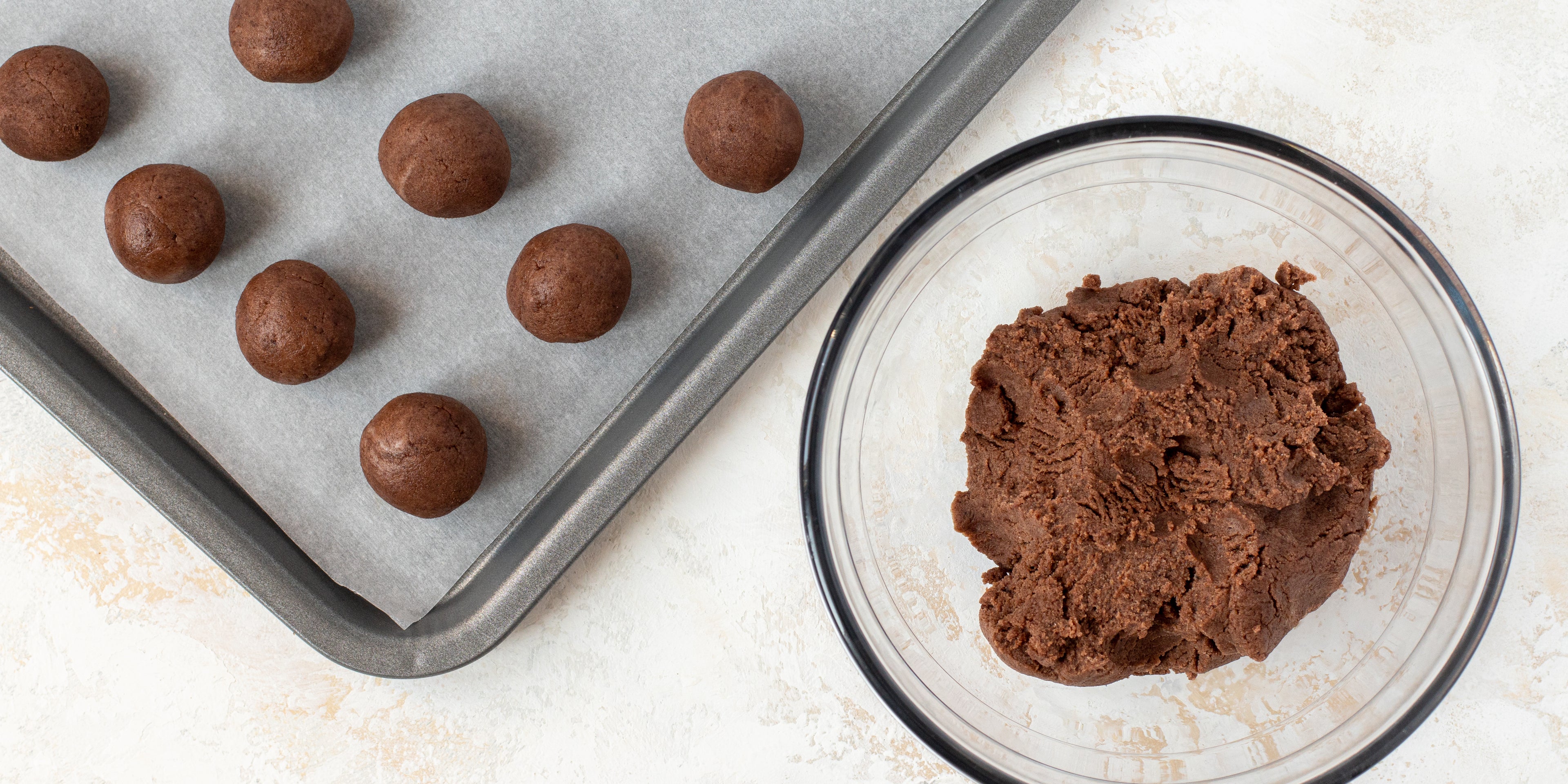 Top view of a glass bowl of chocolate cake being rolled into Chocolate Cake Pops balls on a tray with baking paper