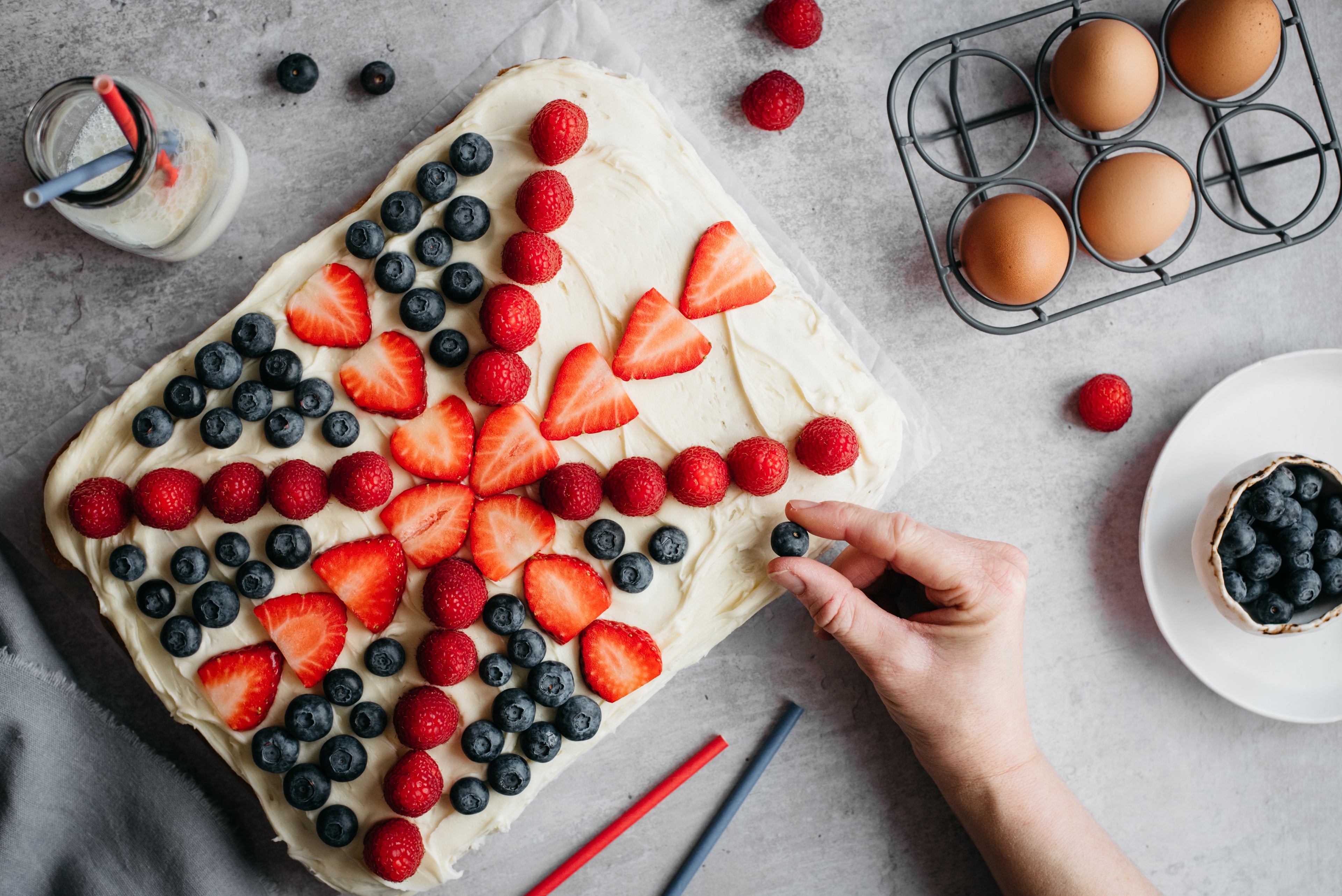 Hands decorating a Union Jack Traybake with fresh berries, perfect for a summer Jubilee party