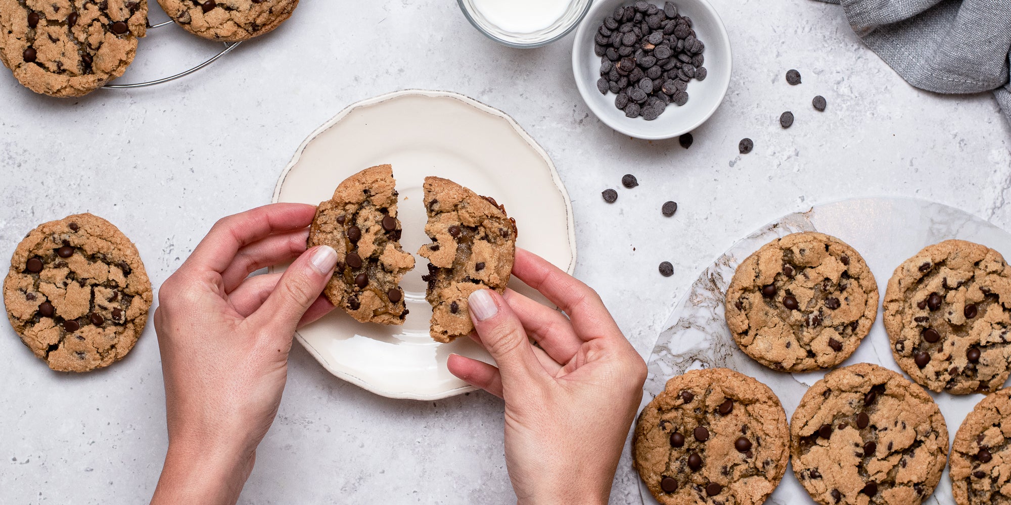 Top down view of some hands breaking a vegan and gluten free chocolate chip biscuit in half