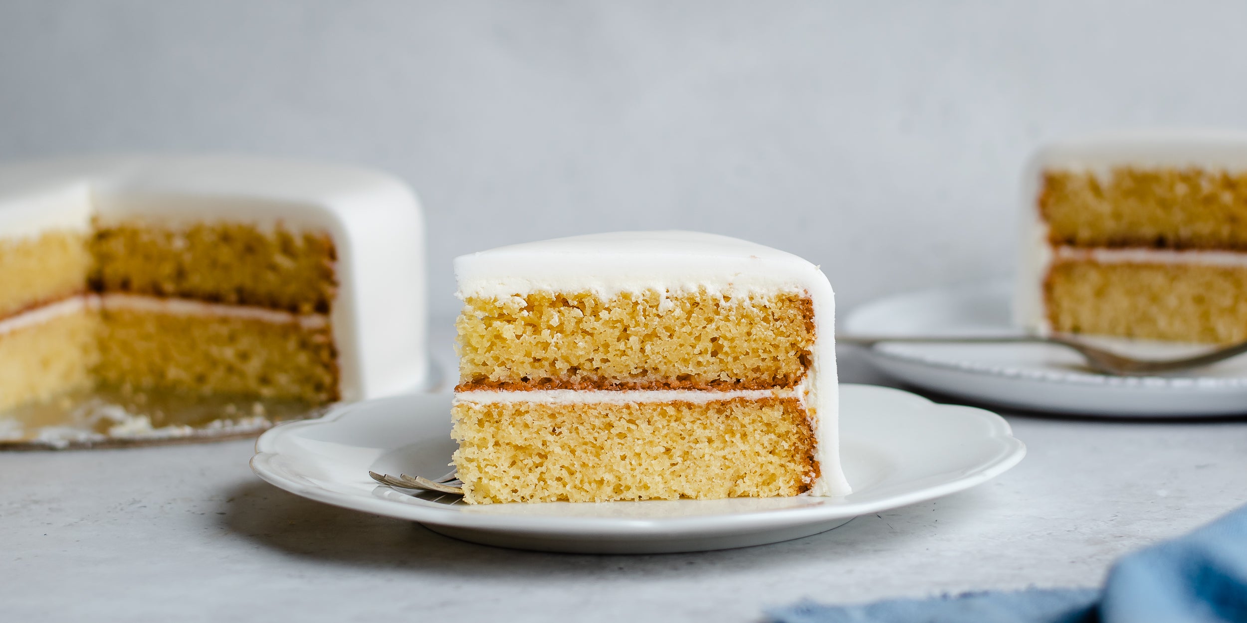 Slice of fondant covered sponge cake layered with jam on plate with remaining cake in background