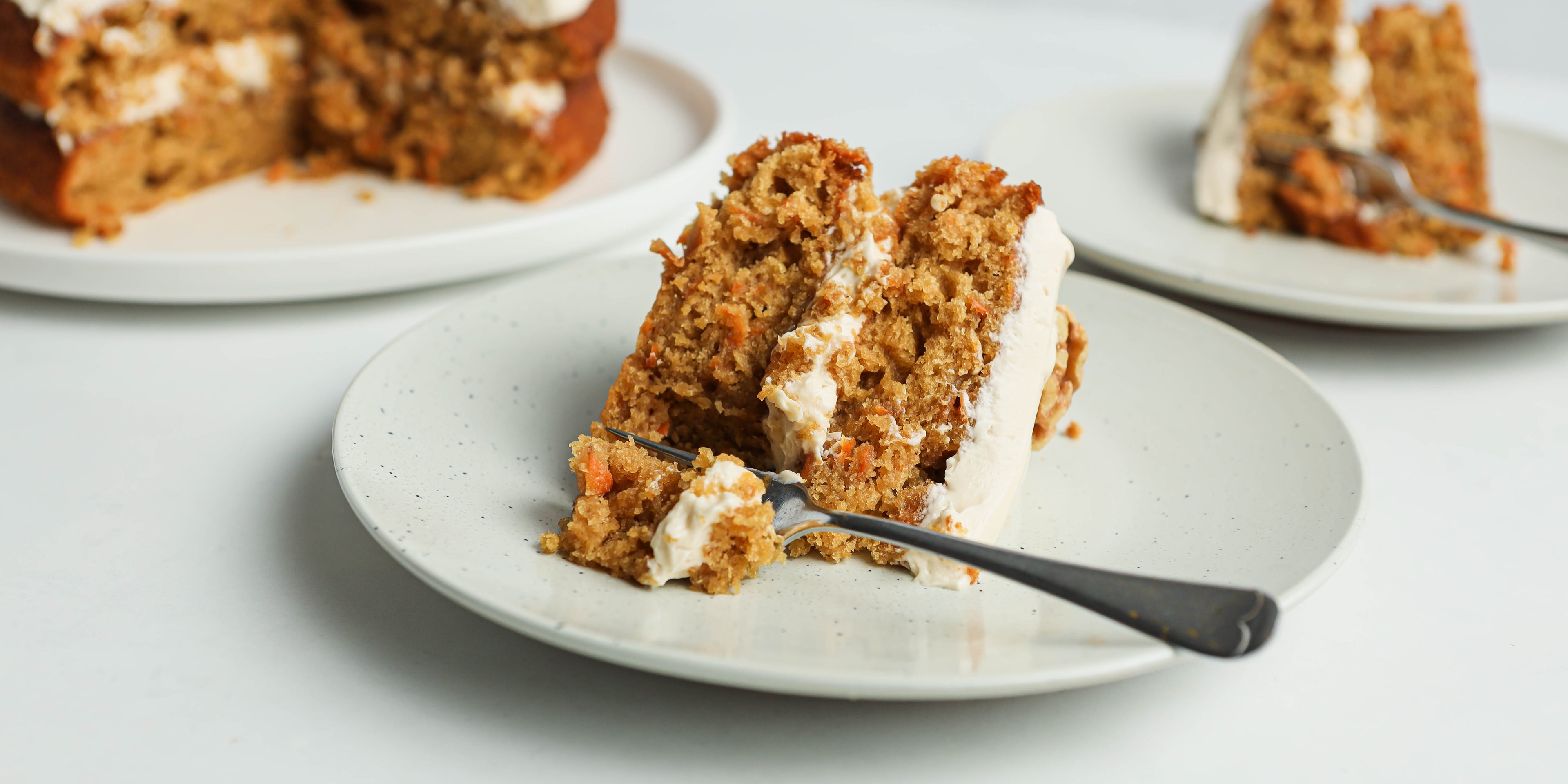 Close up of a slice of Classic Carrot Cake on a plate with a fork cutting into it