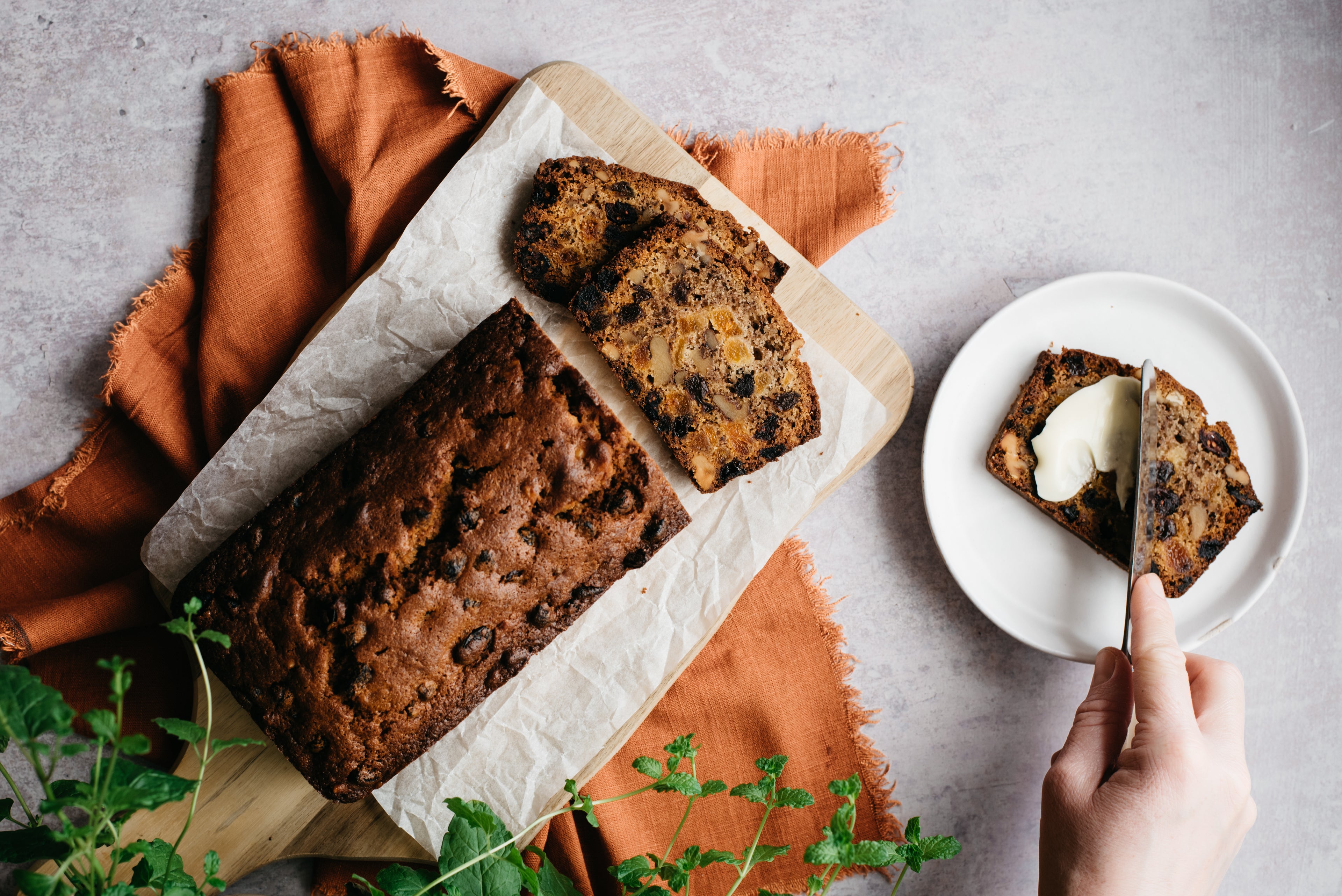 Light fruit cake with a hand buttering a single slice on a plate