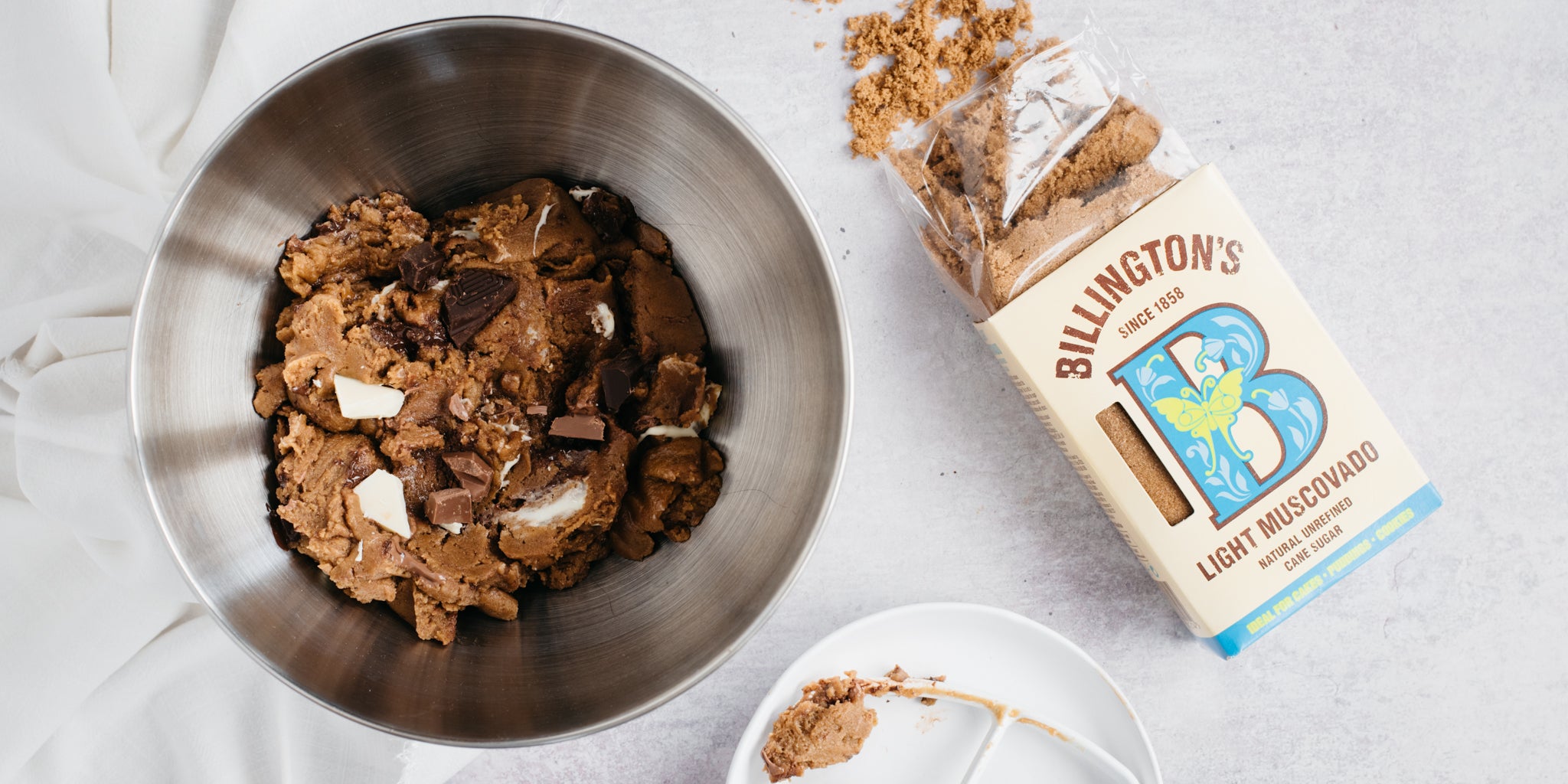 Bowl of cookie mixture with an open pack of sugar spilt beside it