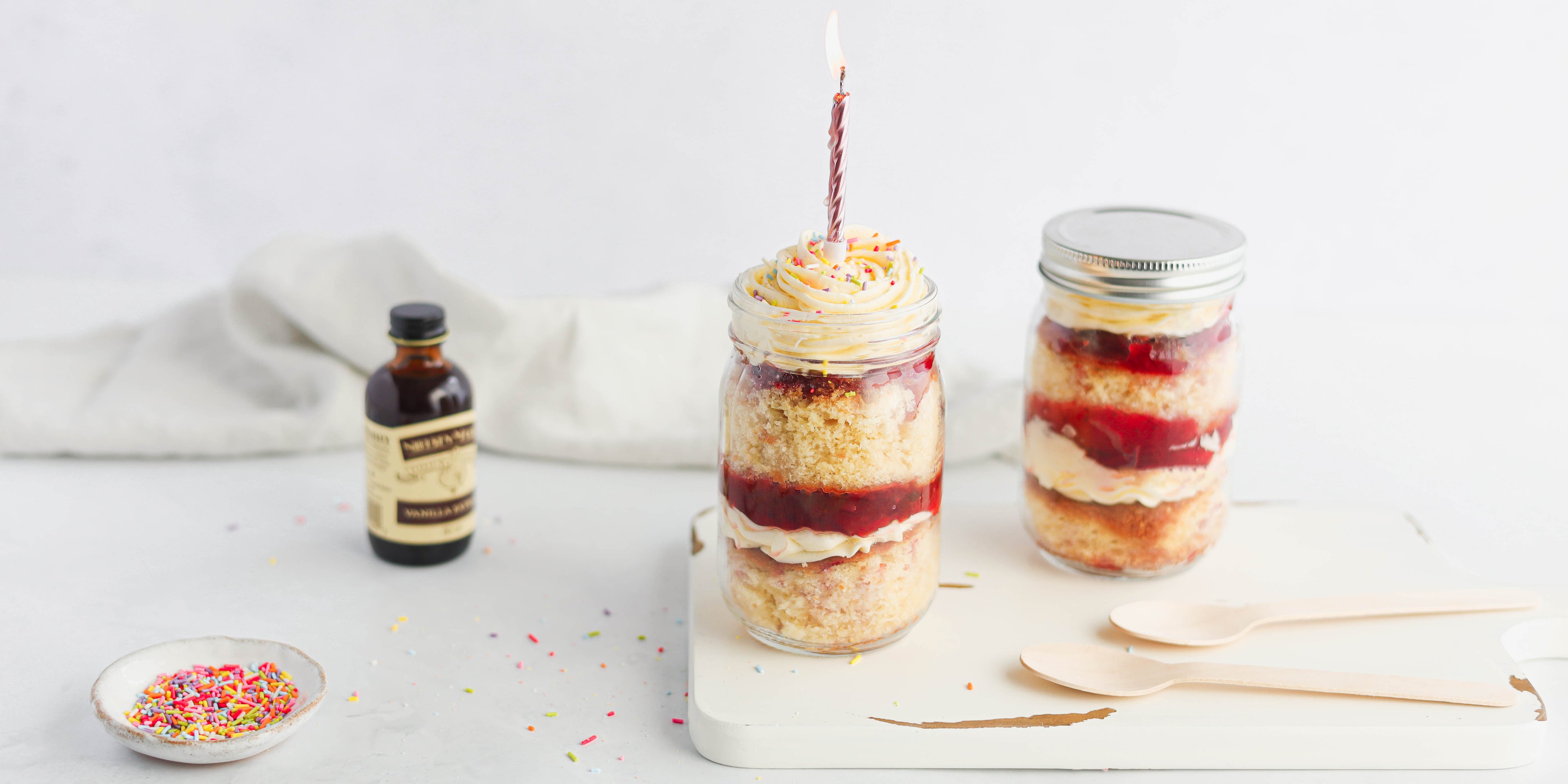 Vanilla Cupcakes in a Jar with a birthday candles and a bottle of Neilsen-Massey vanilla extract