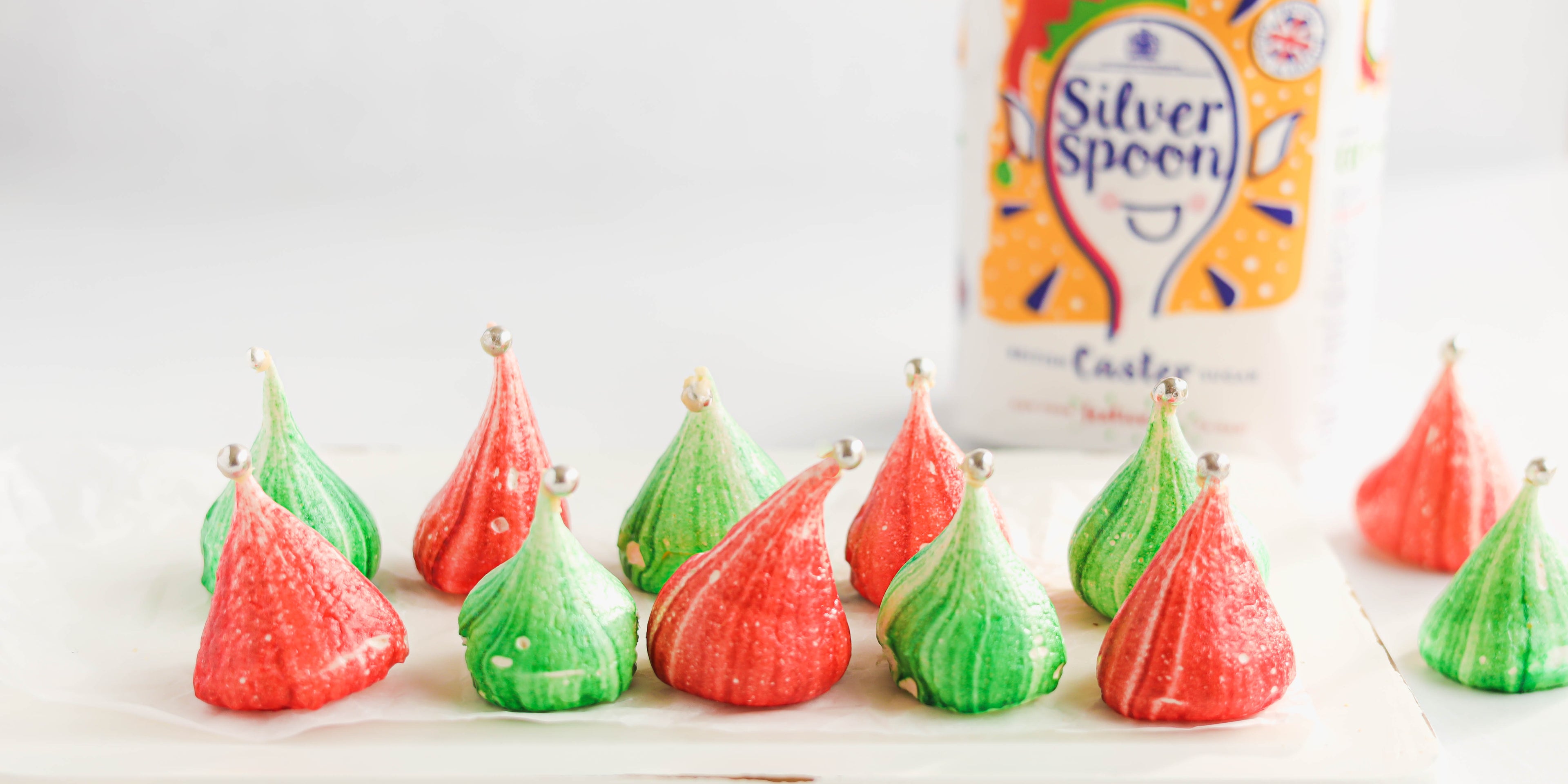 Red and green Rainbow Meringues on parchment paper with silver spoon caster sugar pack in the background