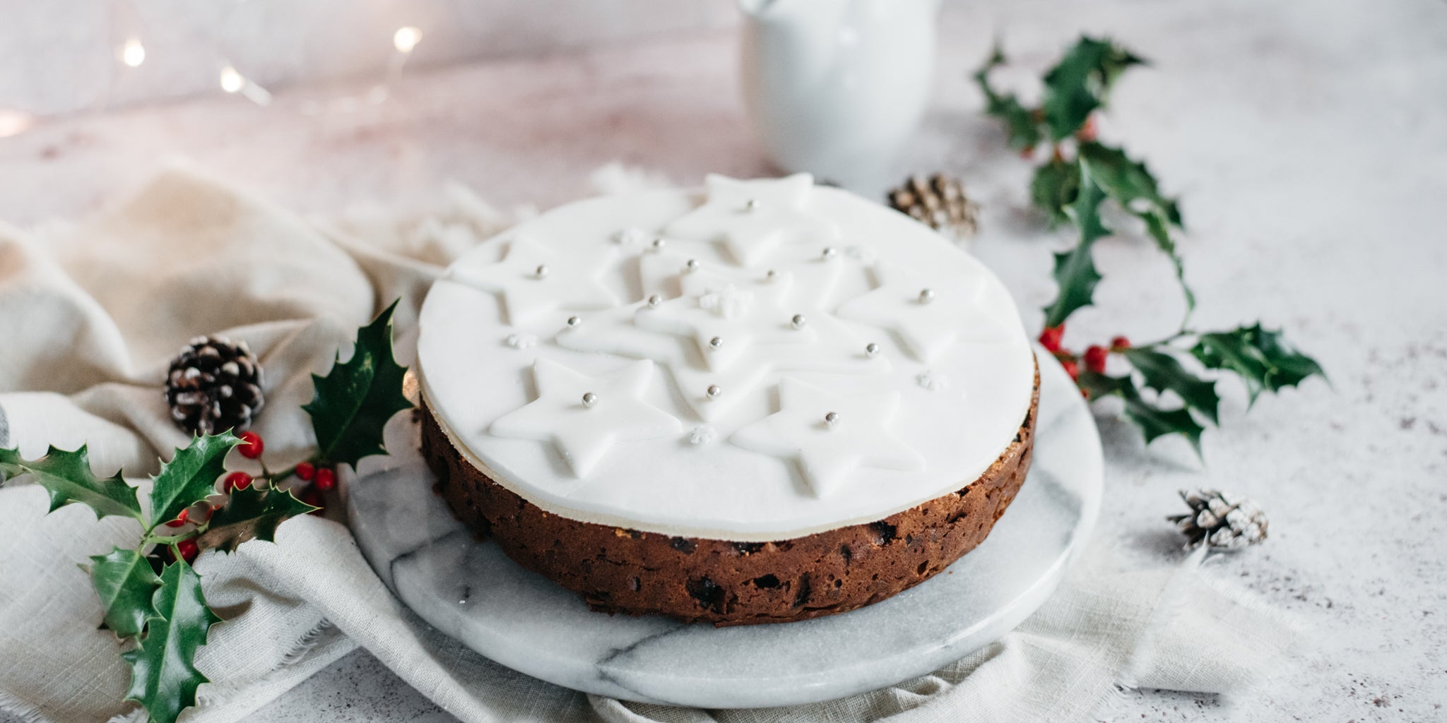 Fruit cake decorated with white icing and stars, surrounded by holly and pine cones