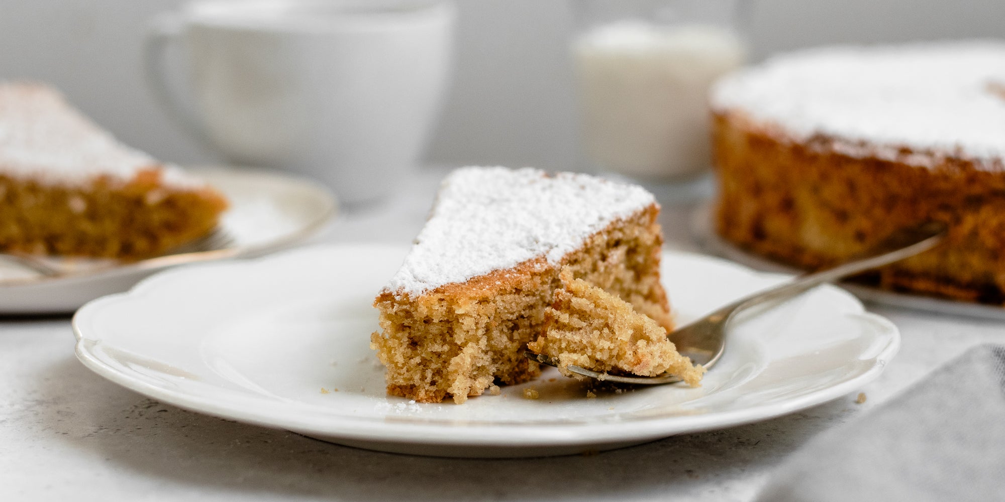 Close up slice of Tarta de Santiago dusted with icing sugar, on a plate with a fork with a bite taken out of it