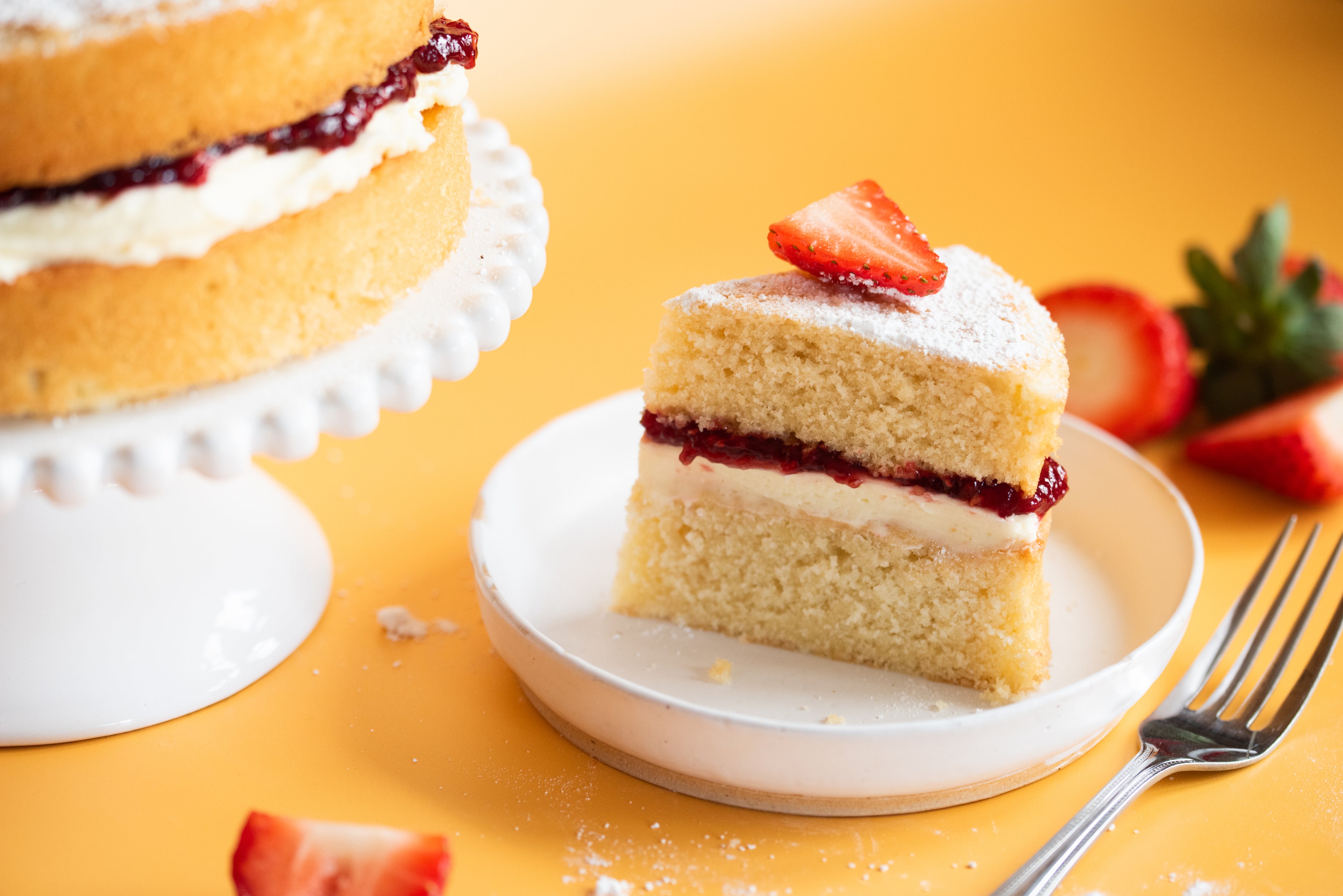 Close up of a slice of victoria sponge on a plate with a fork beside it