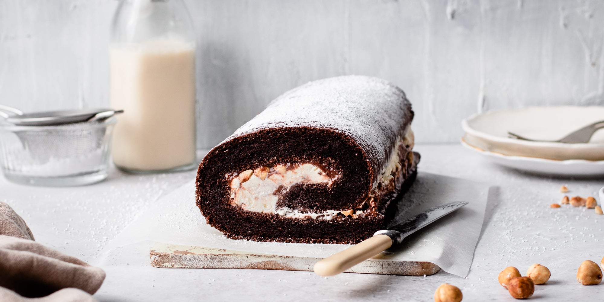 Chocolate Roulade ready to serve on a serving board, next to a knife. With a bottle of milk in the background