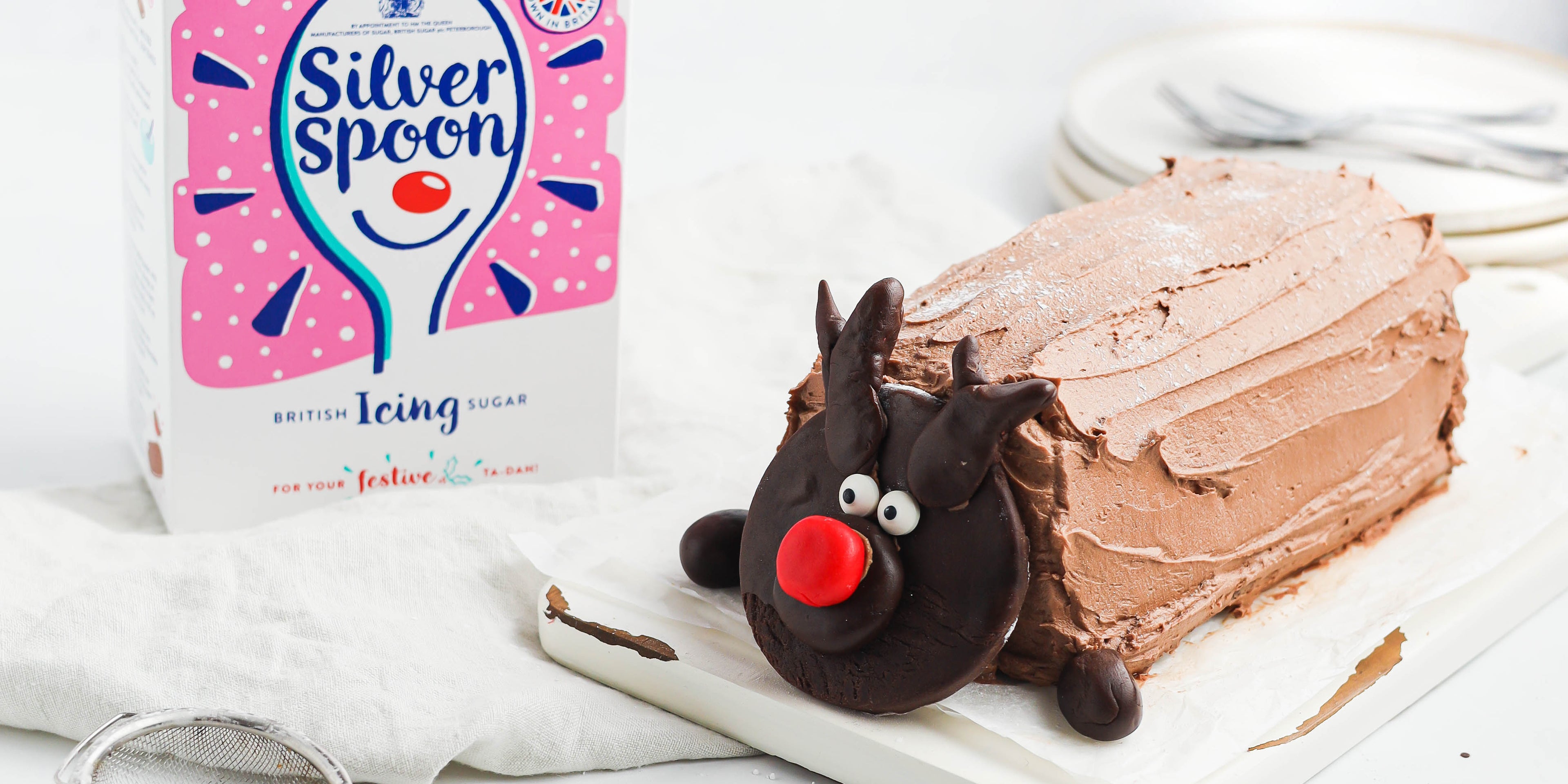 Chocolate Yule Log with a chocolate reindeer face made out of dark chocolate next to a a box of Silver Spoon Icing Sugar