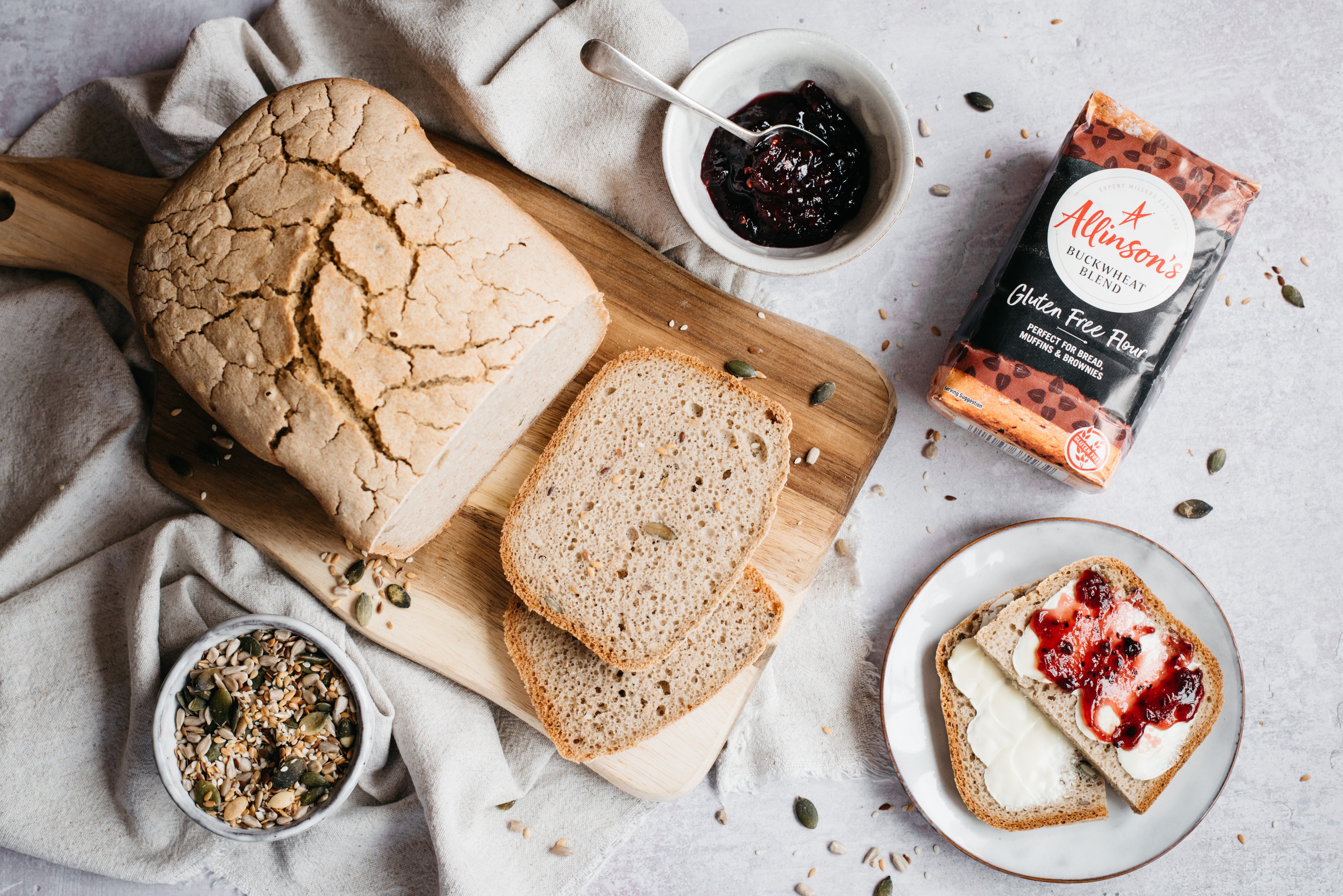 Gluten Free loaf with slices laid infront, flour pack, bowl of seeds and jam