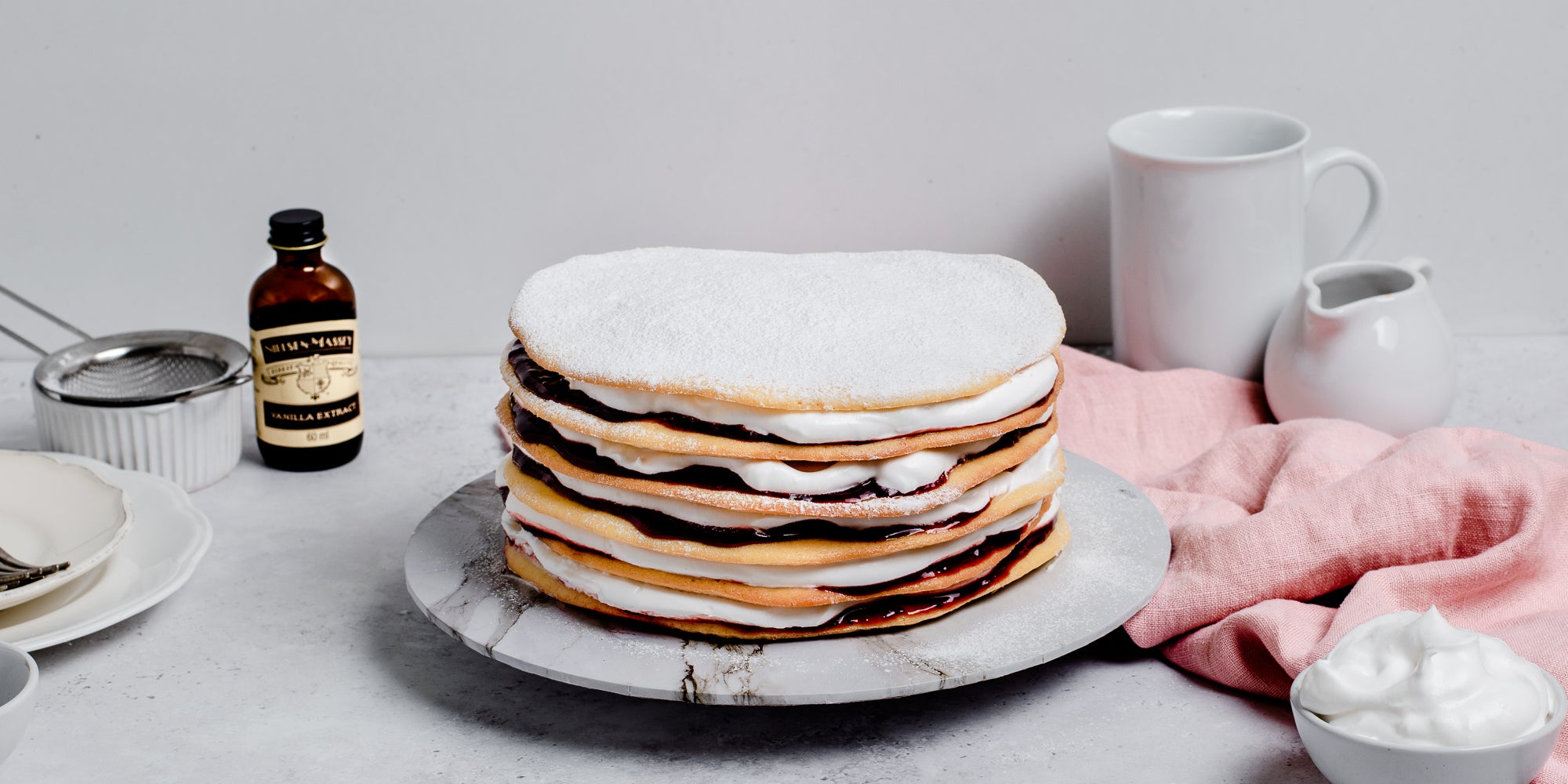 Danish Layer Cake served on a marble plate, with a sieve and a bottle of Nielsen-Massey Vanilla Extract in the background